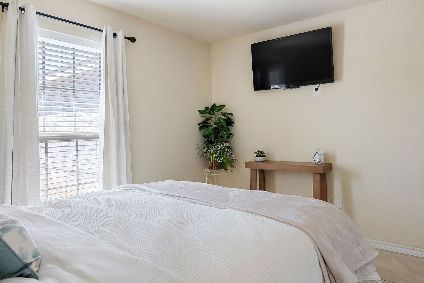Enter this inviting bedroom equipped with a mounted TV, lush greenery, and a modern wooden console.