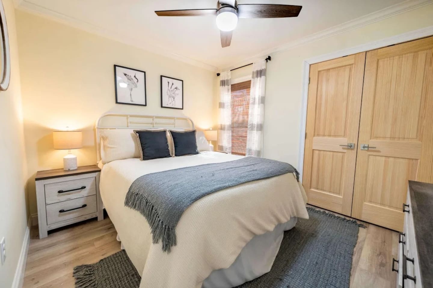 Upstairs bedroom with a queen-size bed dressed in soft, neutral tones, a wall-mounted smart TV, and a dresser for personal storage. A ceiling fan and bedside lighting add comfort and functionality. Simple, inviting, and easy to settle into.

