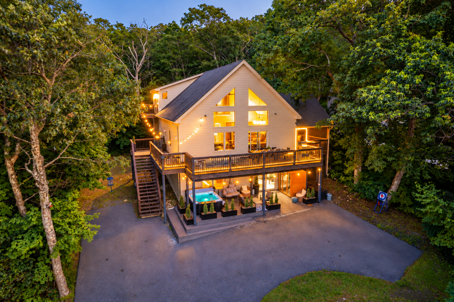 Twilight drone view showcases the home’s glowing deck lighting, multiple outdoor zones, and tree-wrapped privacy just steps from the Blue Ridge Parkway