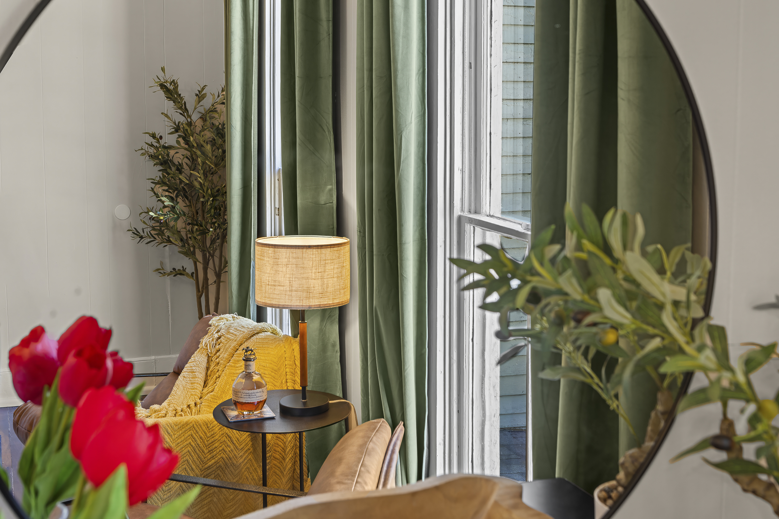 A round mirror, red tulips, and a leather chair in the corner.
