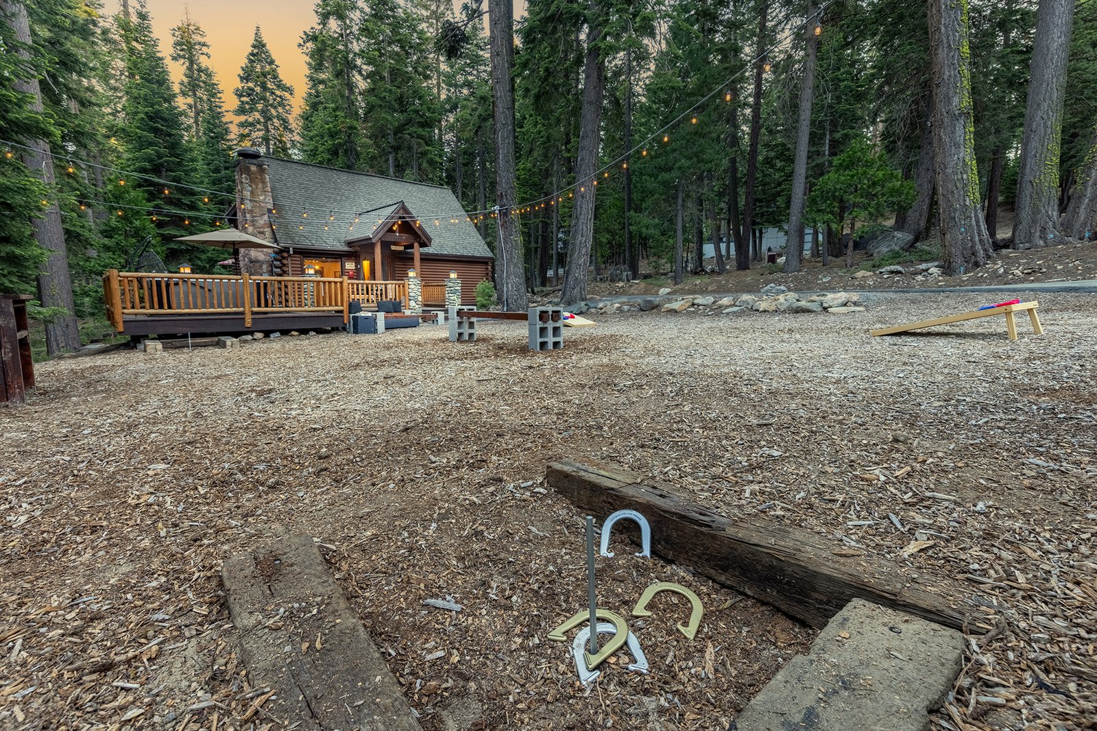 Run a backyard tournament till the lights take over — horseshoes, cornhole, and ladder golf all set up in the clearing.