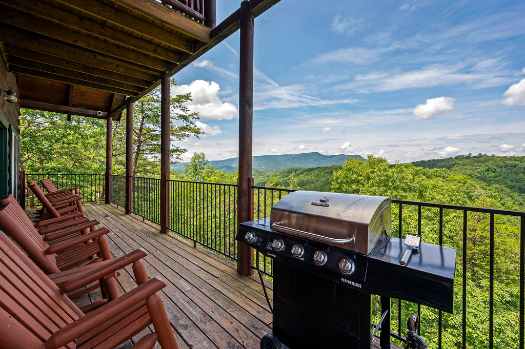 Wooden deck with rocking chairs for relaxation, a sleek grill, and majestic views