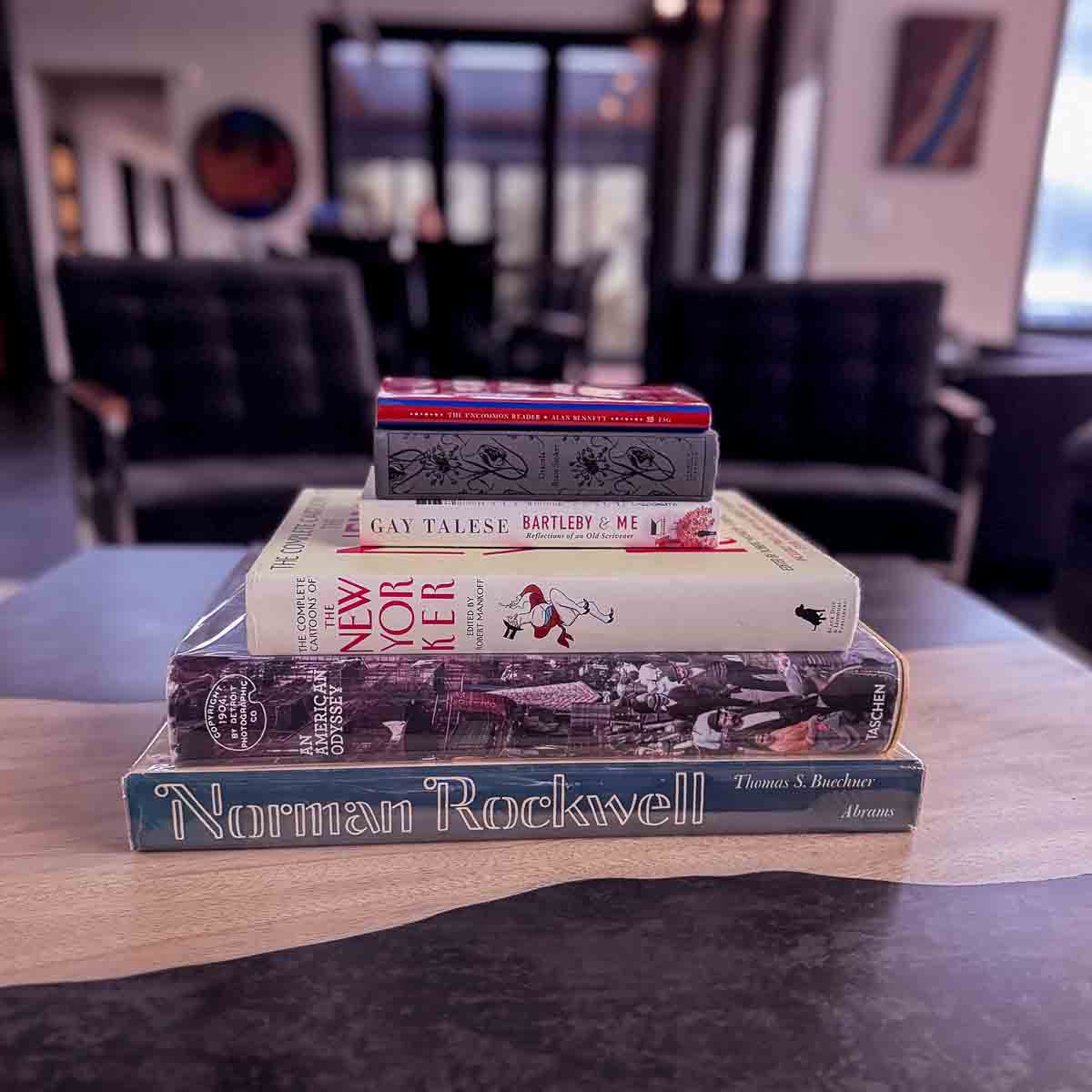 Curated stack of books on the coffee table &mdash; Norman Rockwell, New Yorker cartoons, Gay Talese &mdash; Sunset Falls Berkshires