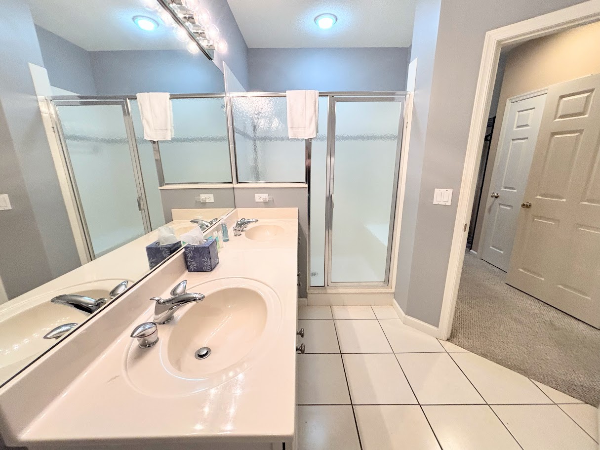 Bright bathroom with a large vanity, full mirror, tile flooring, and walk-in shower with glass doors.