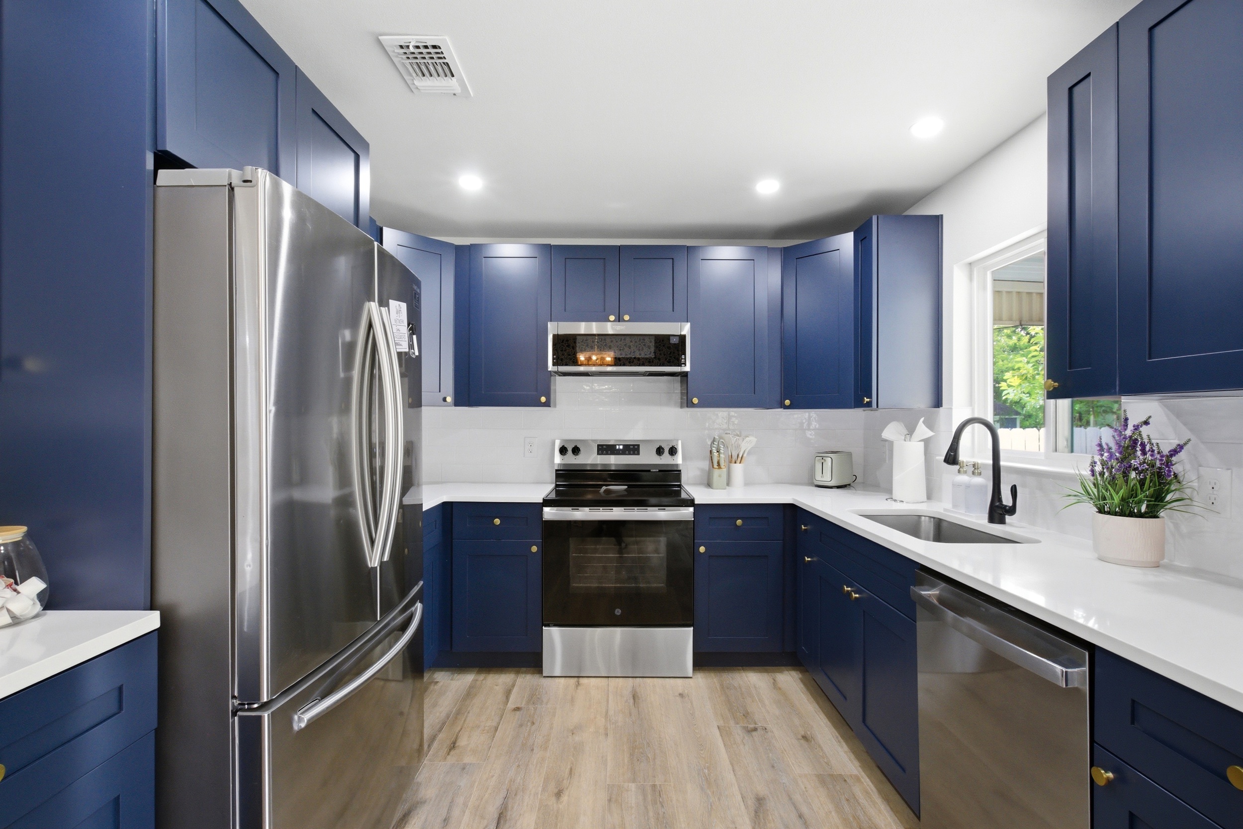 Fully Equipped Kitchen with Navy Cabinets, Stainless Appliances, Samsung Refrigerator, GE Electric Stove, and Dishwasher. Cookware, Dishes, and Cooking Basics provided.
