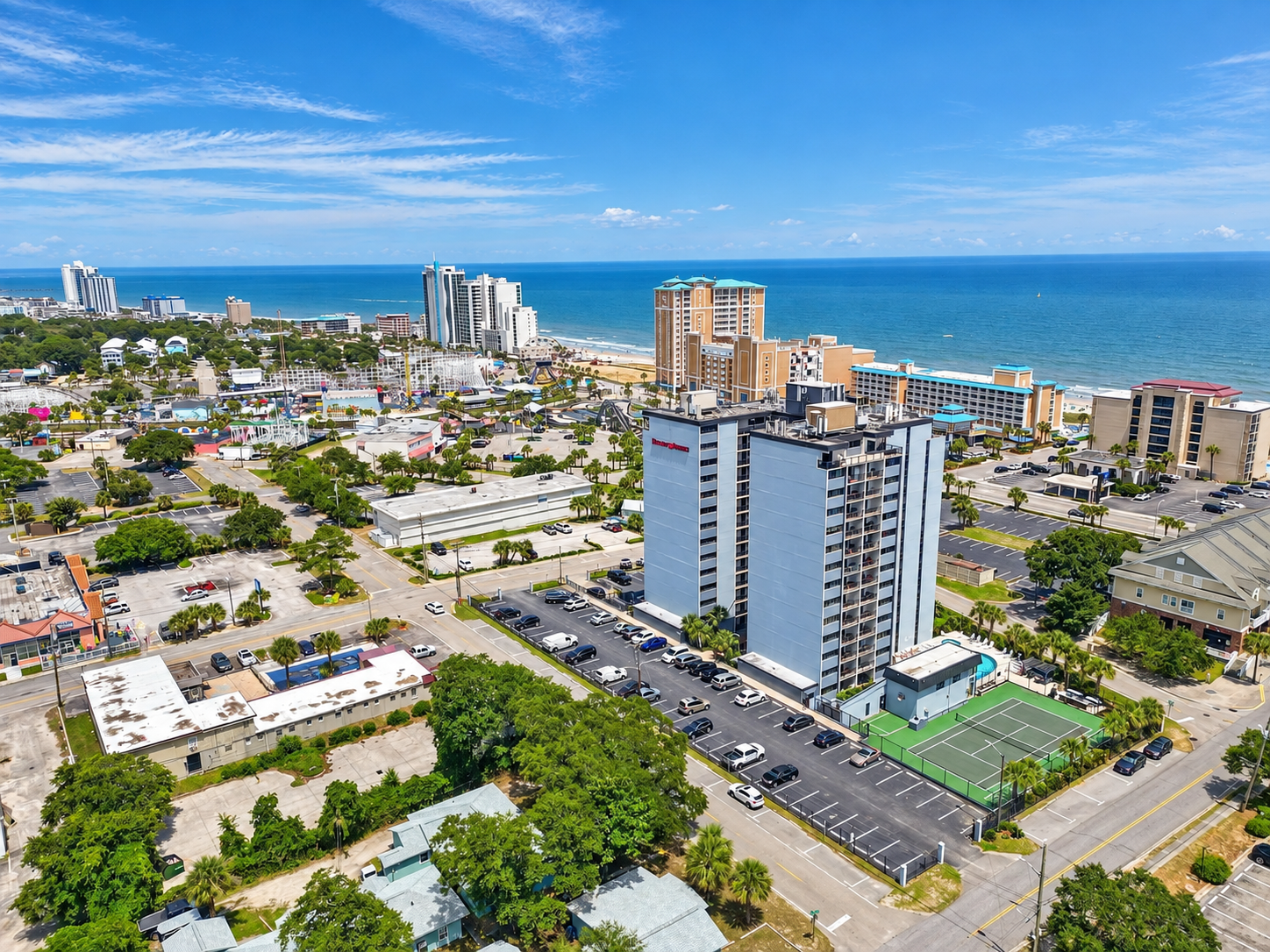 Aerial view of Holiday Towers with shared pool, hot tub, sports court, parking, and Myrtle Beach attractions nearby.