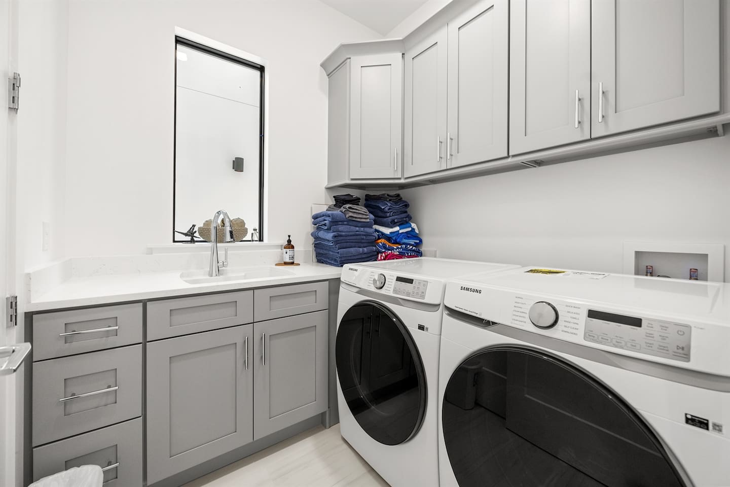 Explore the laundry area featuring an automatic washing machine, sleek cabinet countertops, a stylish granite table, and convenient drawers underneath, combining functionality and modern design for your convenience.