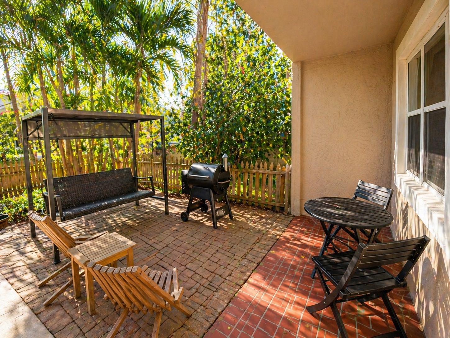 backyard with smoker, grill, swinging chair and fenced yard with Christmas lights at night 