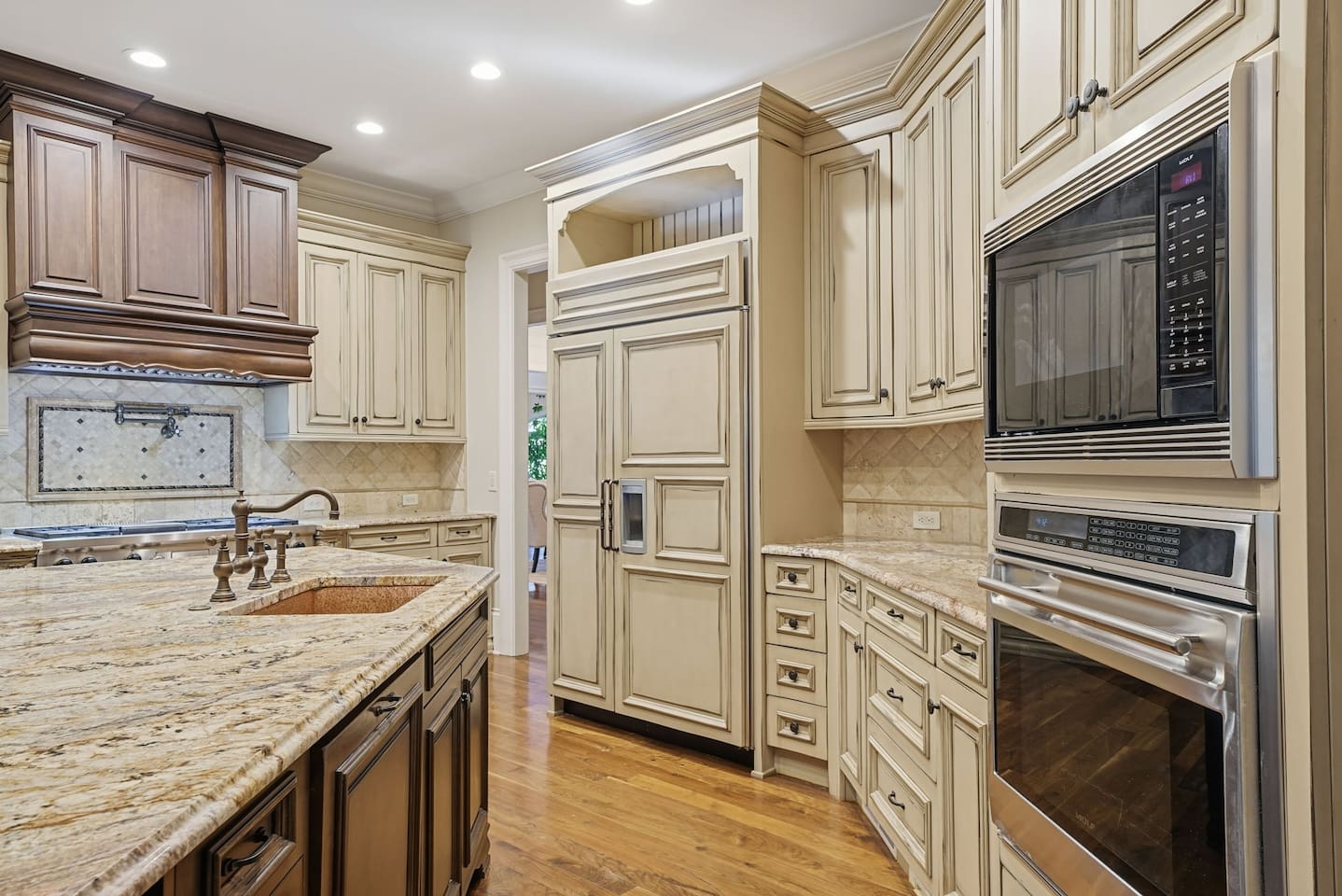 This open kitchen features beautiful cream wood cabinetry, sleek granite countertops, and an island that comfortably seats four. The bright, airy design makes it the perfect place to cook, gather, and share meals together.