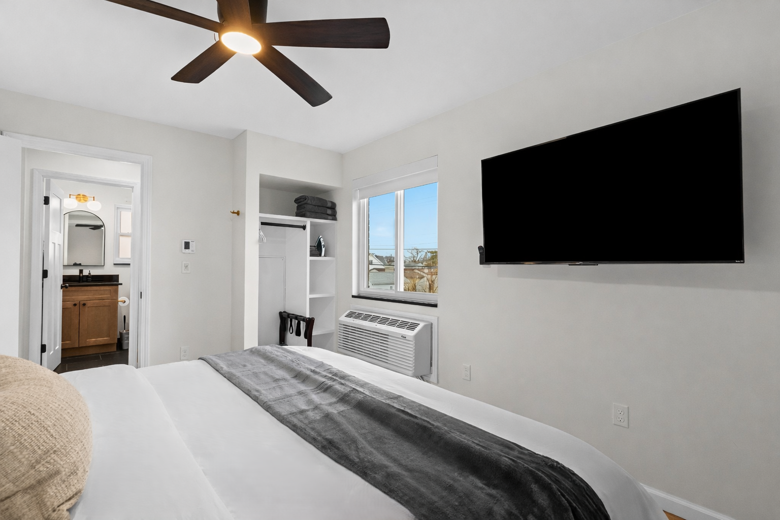 Relaxing bedroom retreat with plush bedding, ceiling fan, smart TV, and bright window—designed for comfort, convenience, and restful nights.