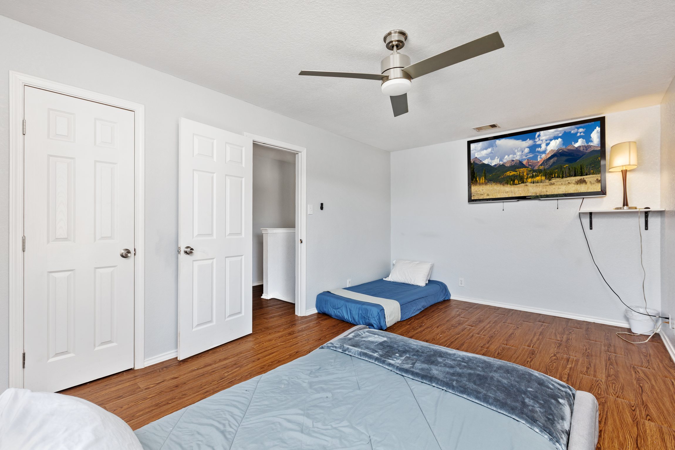 Queen and twin bedroom with wall-mounted Smart TV, streaming apps, ceiling fan, room-darkening shades, and hotel-quality bedding. Clothing storage and extra pillows included. Current decorative blankets, bedding, and wall art are not shown in these photos.