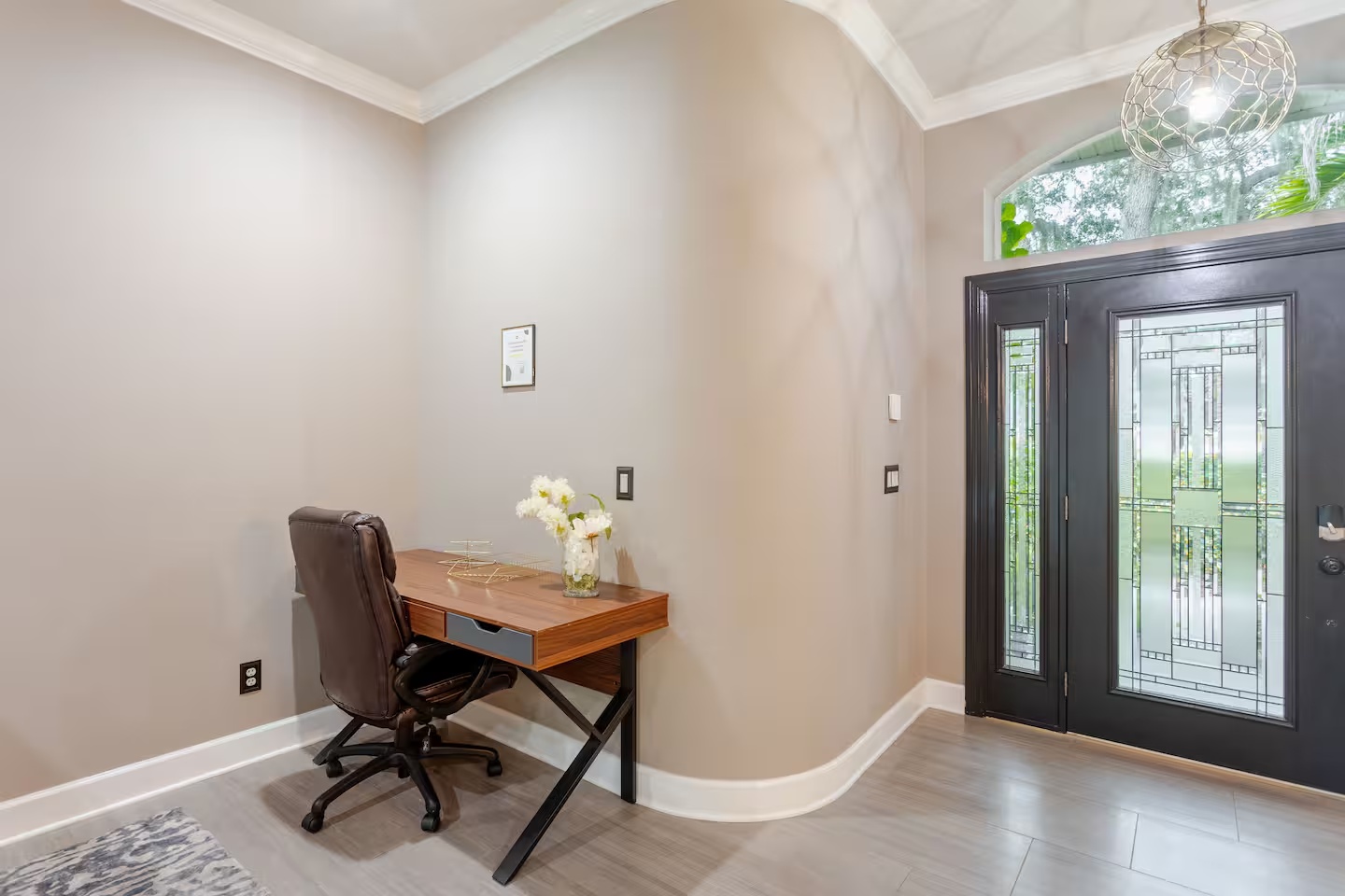 A bright, elegant entryway featuring a stylish wood desk and comfortable office chair, creating a convenient workspace near the home’s beautiful black double front doors.