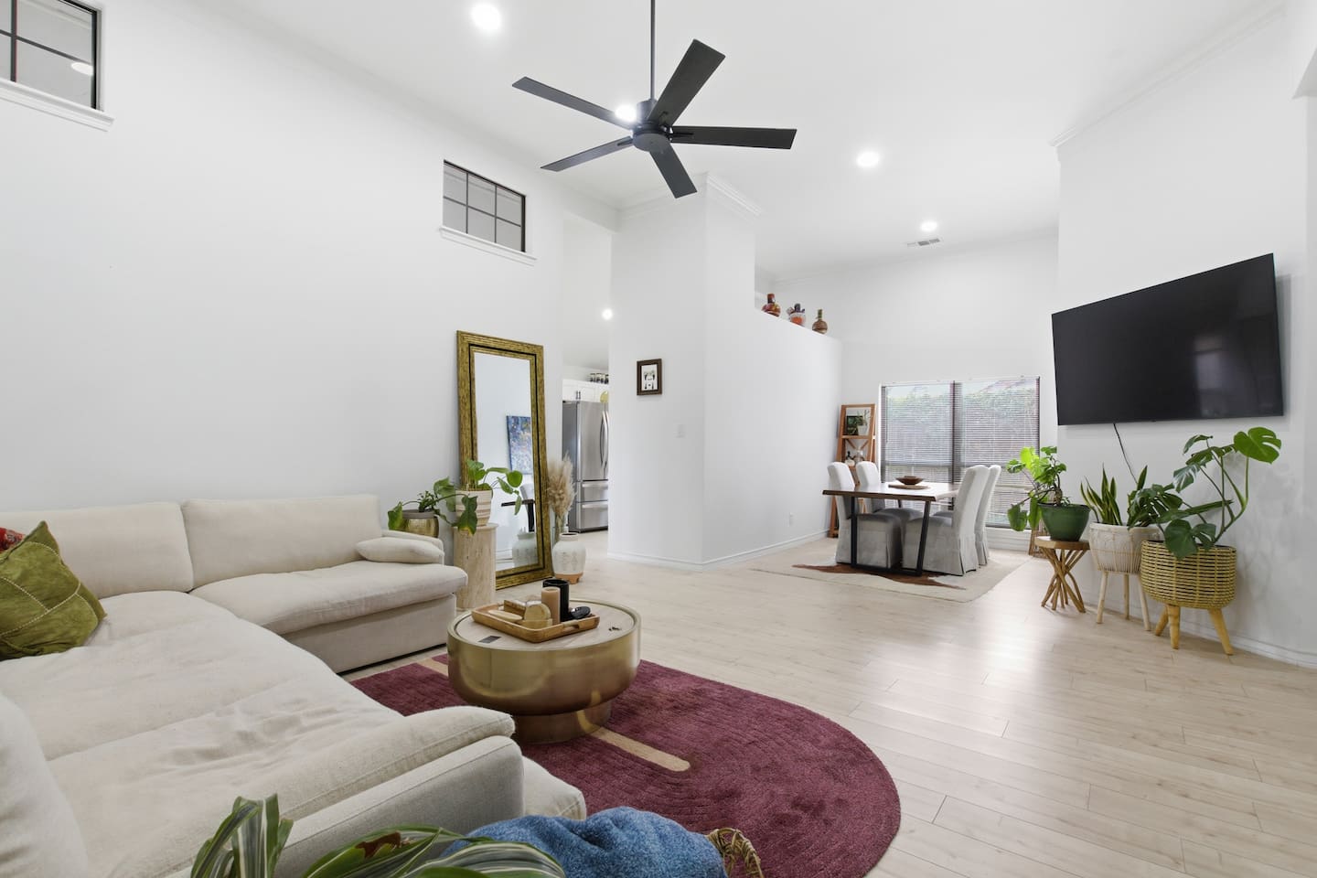 Stylish open living space with Smart TV, cozy sectional, ceiling fan, modern decor, and bright natural lighting for a relaxing stay.