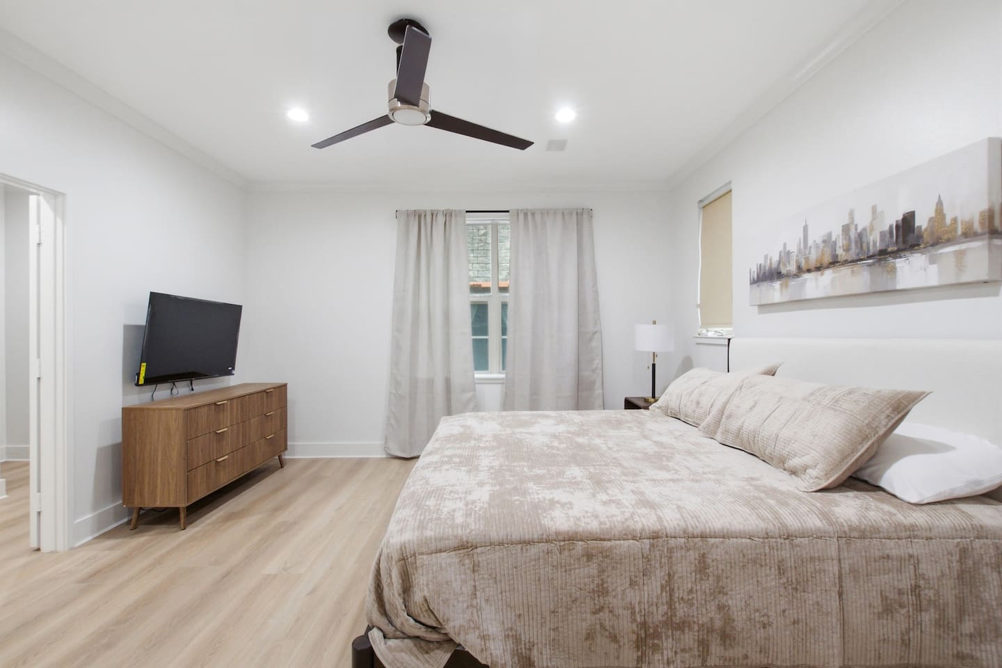 King suite with Smart TV, hardwood floors, and ample natural light throughout the day. The en-suite bathroom with soaking tub and walk-in glass shower is just a few steps away.
