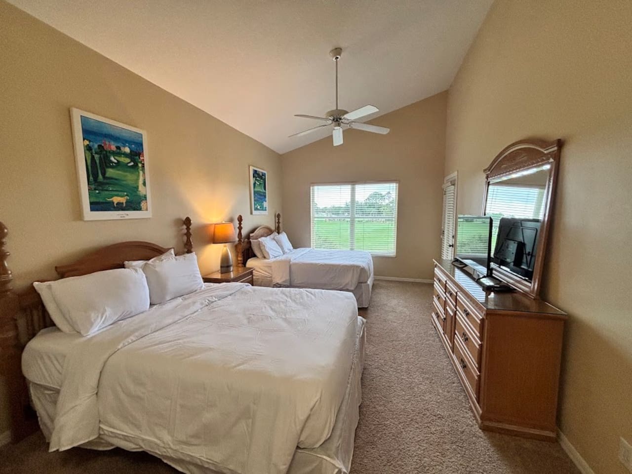 Spacious bedroom featuring two beds, ceiling fan, dresser storage, TV, and natural light.