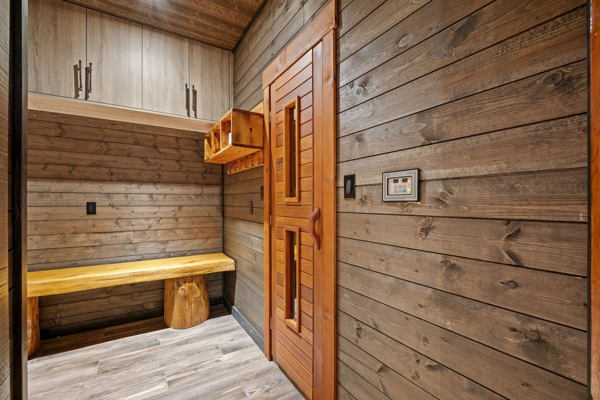 Sauna changing area with handcrafted wood bench, storage cubbies, and digital temperature controls.
