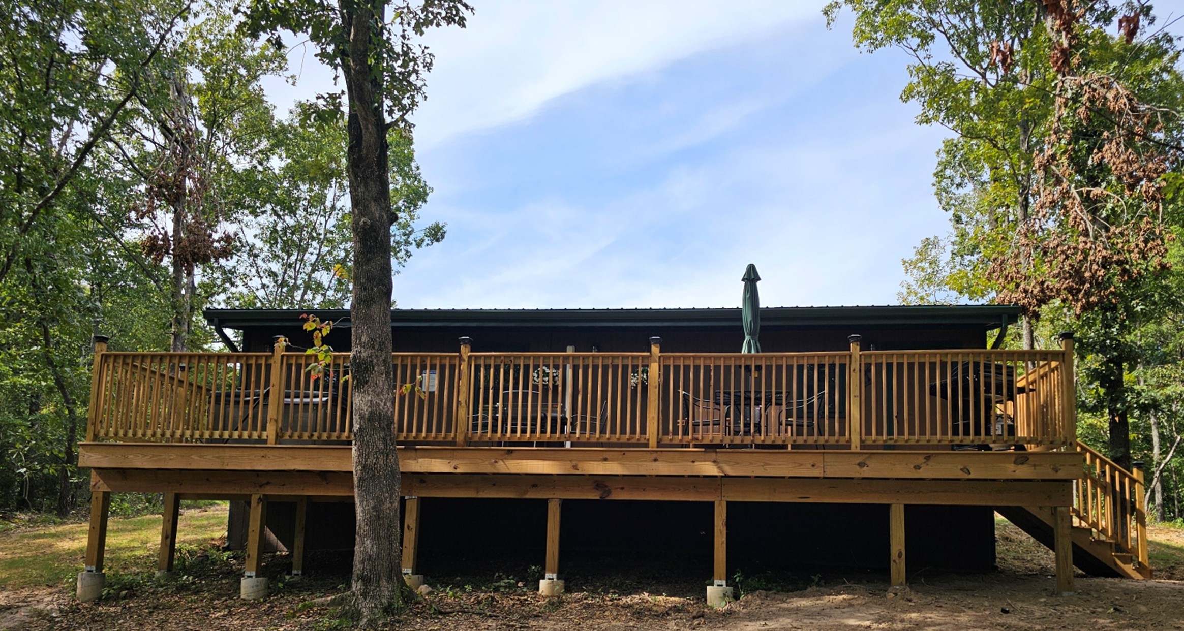Back view of the cabin with a large wooden deck, outdoor seating, and forest setting