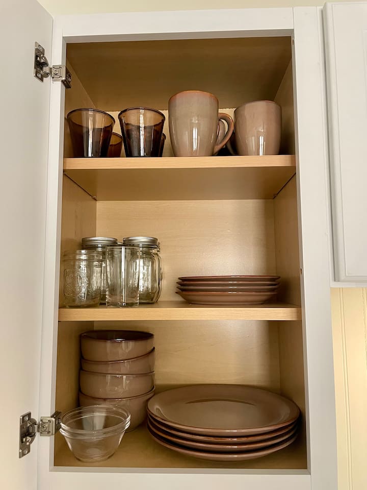 Well-stocked kitchen cabinet with a complete set of dishware, glasses, mugs, and bowls for everyday meals.