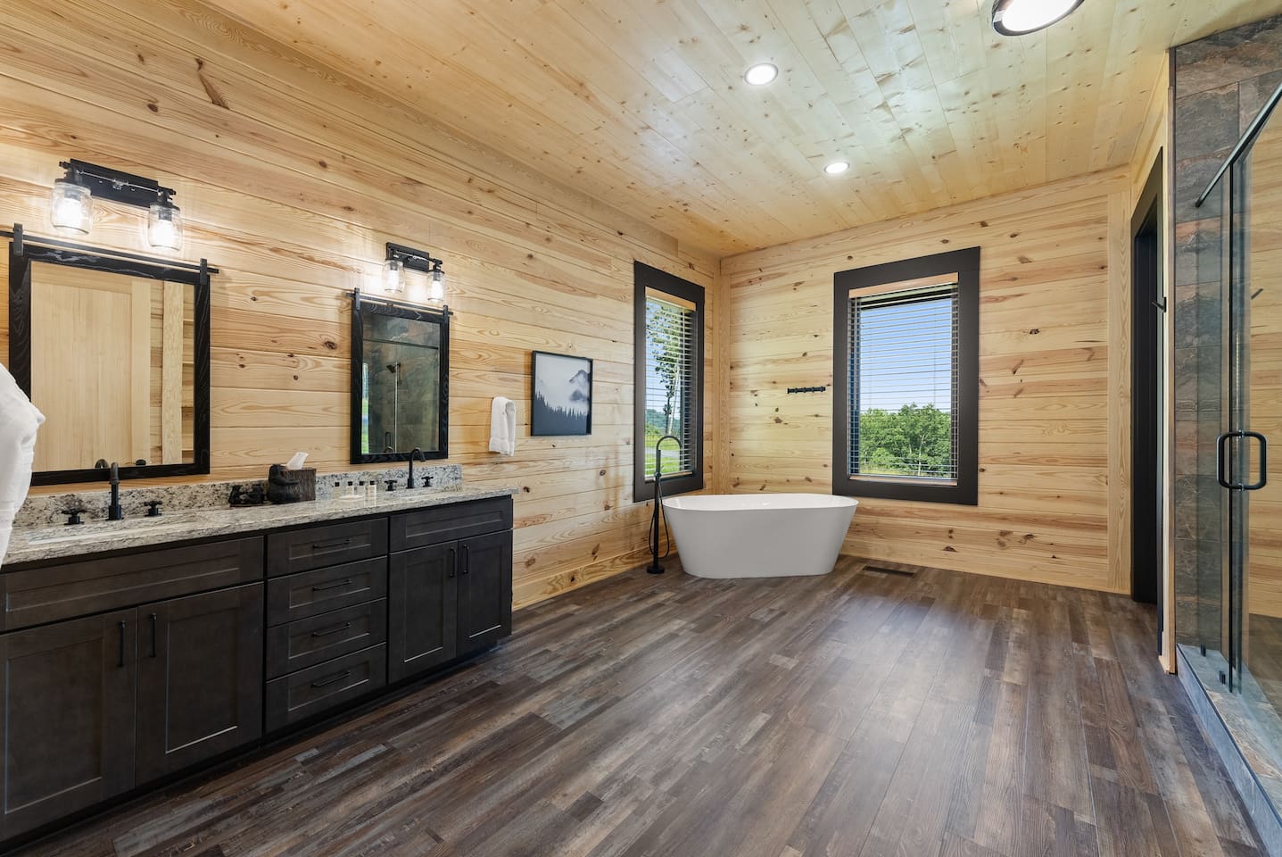 Enjoy the luxury of space in this beautifully designed full bathroom featuring dual vanities, a soaking tub, and serene woodland views.