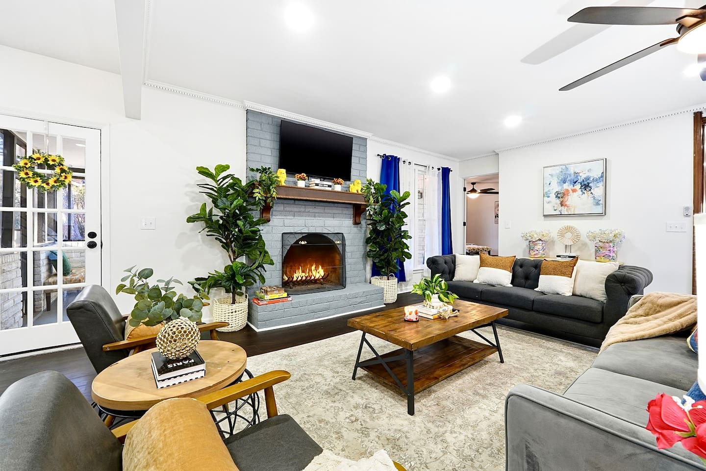 Warm and welcoming living room with two comfortable couches, two chairs, indoor plants, a cozy fireplace, and a TV powered by Google TV. Conveniently located as you walk through the front door and straight ahead from the primary side entrance. 