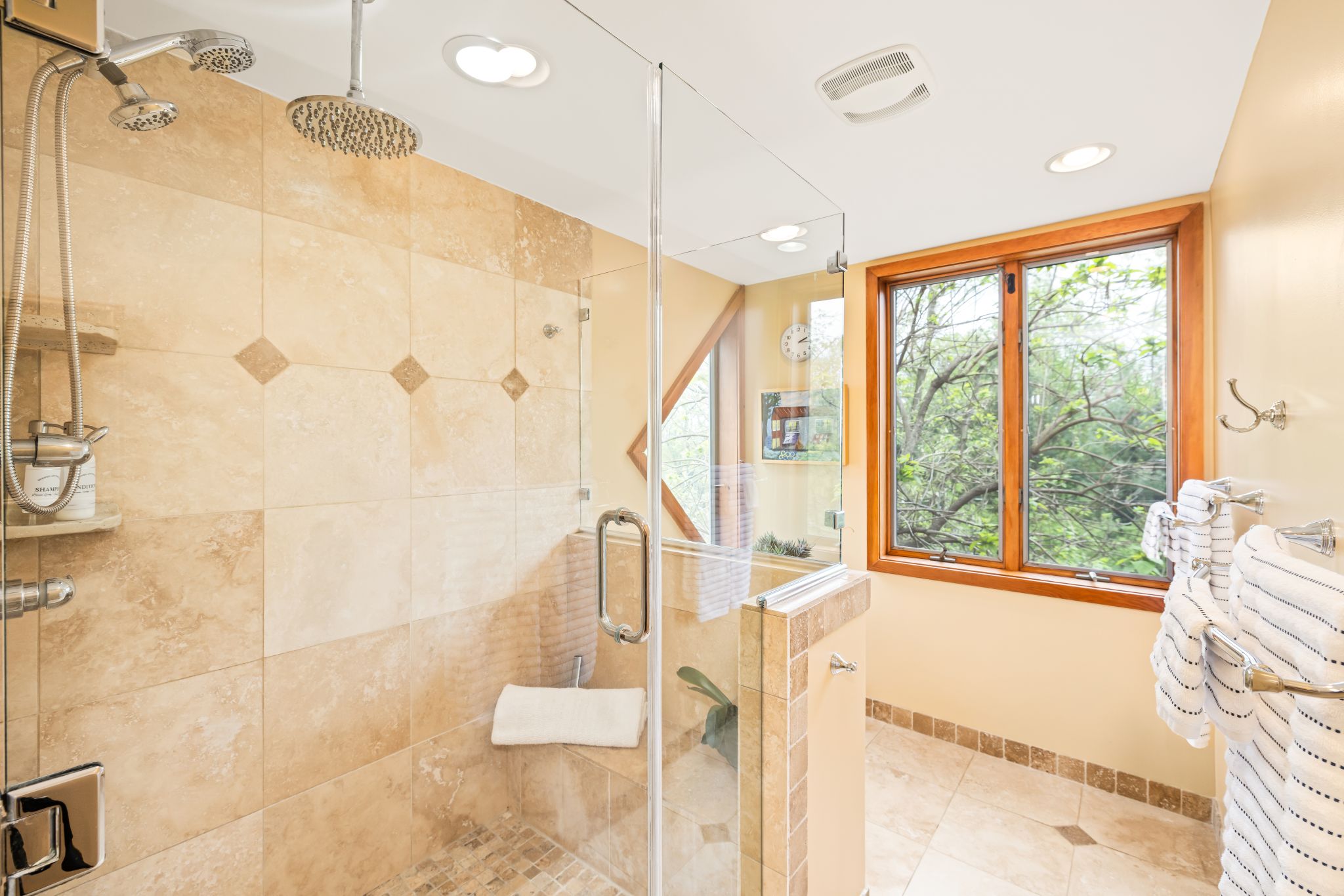 Hilltop Oasis' Mountain View Suite's spa retreat: The primary bath with walk-in shower, dual rainfall heads, and a built-in bench. Enjoy the peaceful forest views for a calm start or end to your day.