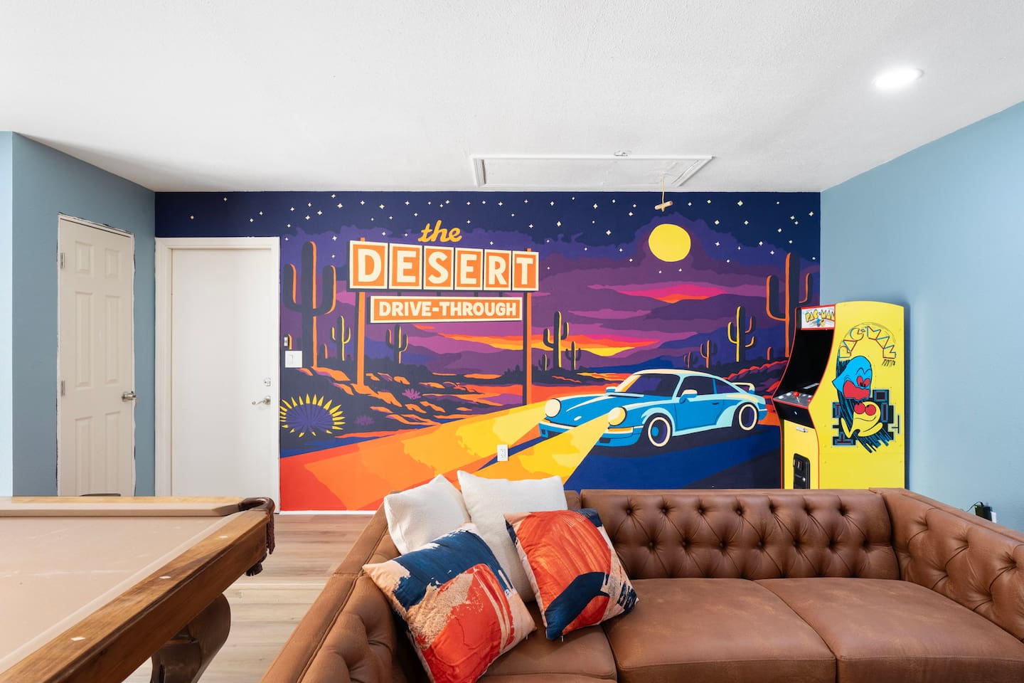 Retro game room with iconic Desert Drive-Through mural, leather seating, pool table, and arcade—nostalgic fun space for all ages.