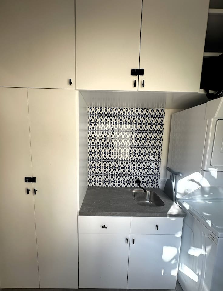 Discover our custom-built laundry and sink, designed to meet all your clothes care needs, complete with a clothes drying rack, ladder, mops, and brooms conveniently stored behind the door.