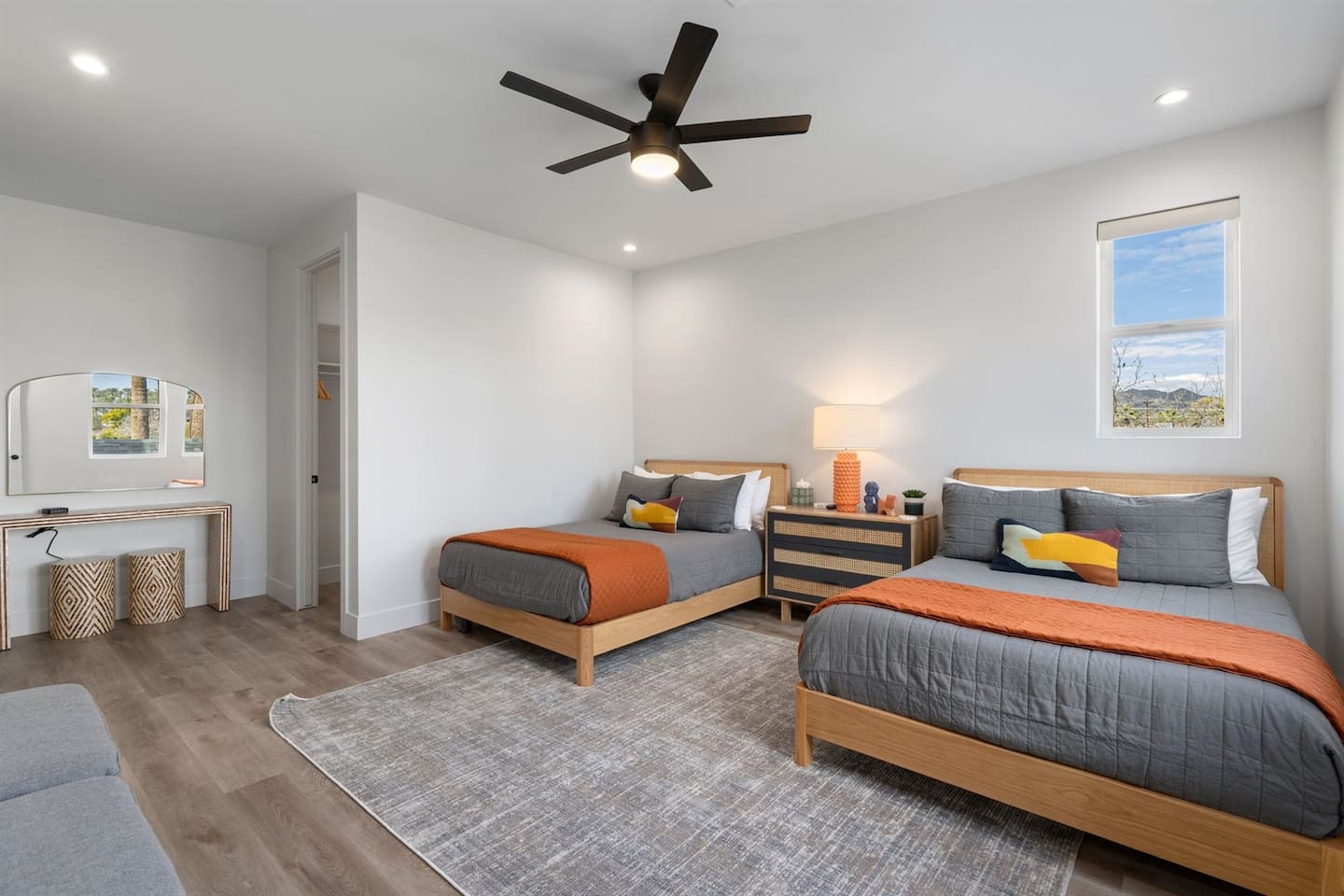 Enjoy relaxation in this spacious bedroom with two double beds, a bedside table, a ceiling fan, and a TV, complemented by a stylish vanity area and a private bathroom for a pleasant stay.