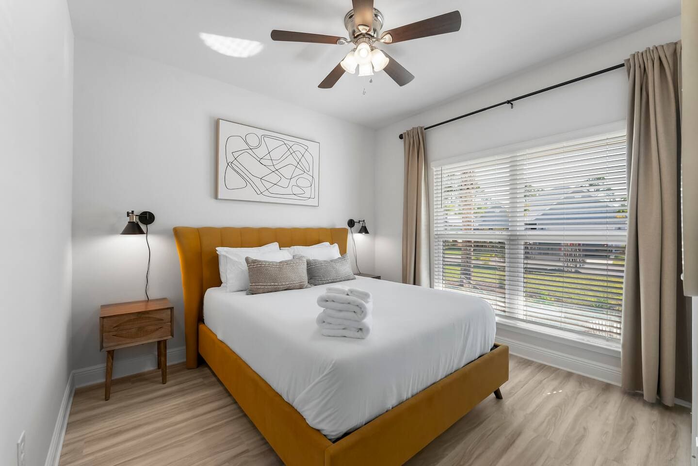 Charming bedroom with sunny windows, bedside lamps, ceiling fan mirror, and artistic accents.