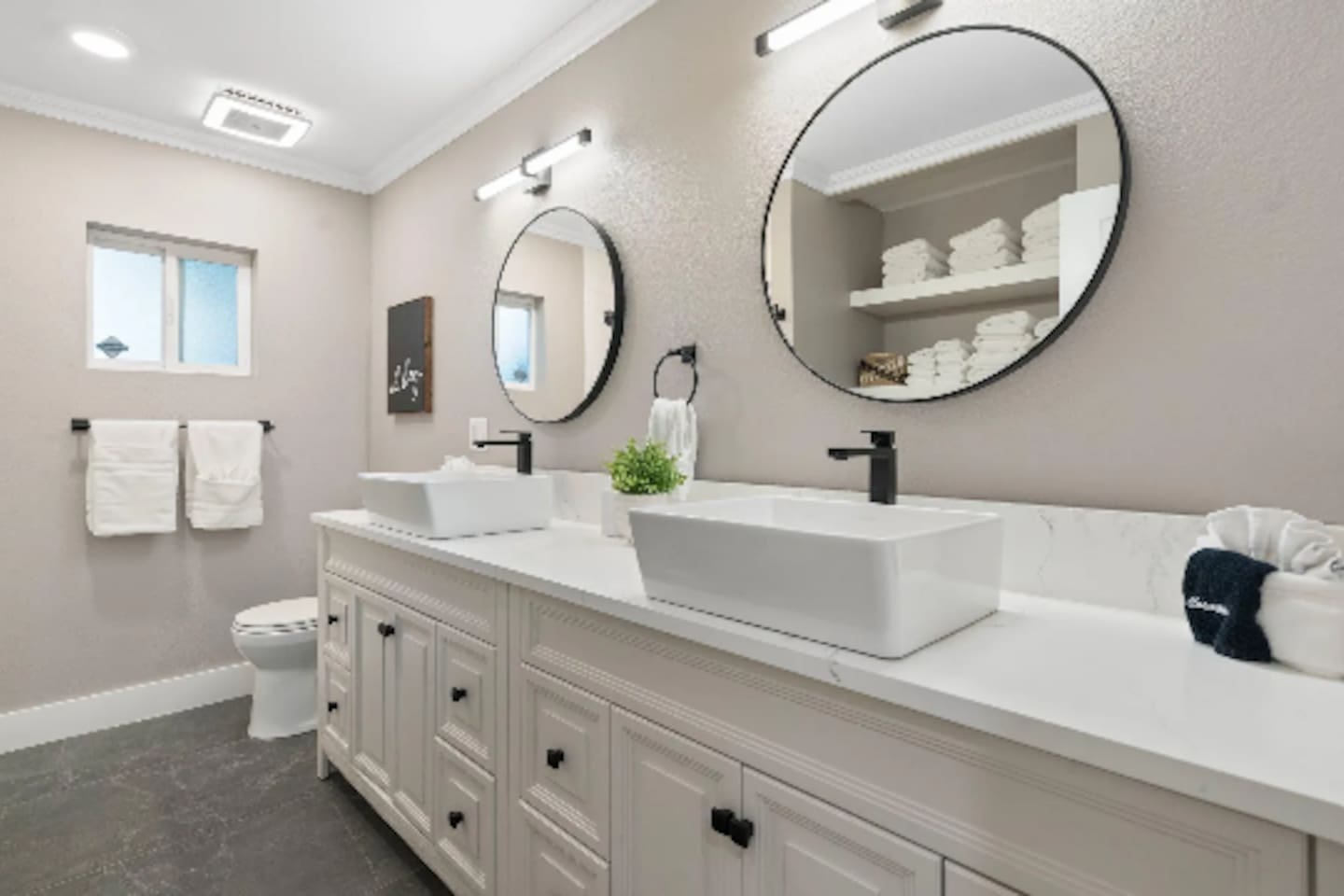 A long dual vanity with vessel sinks gives this bathroom plenty of room to spread out, while round mirrors and stacked fresh towels add a spa-like finish. Natural light from the window keeps the space feeling bright throughout the day.