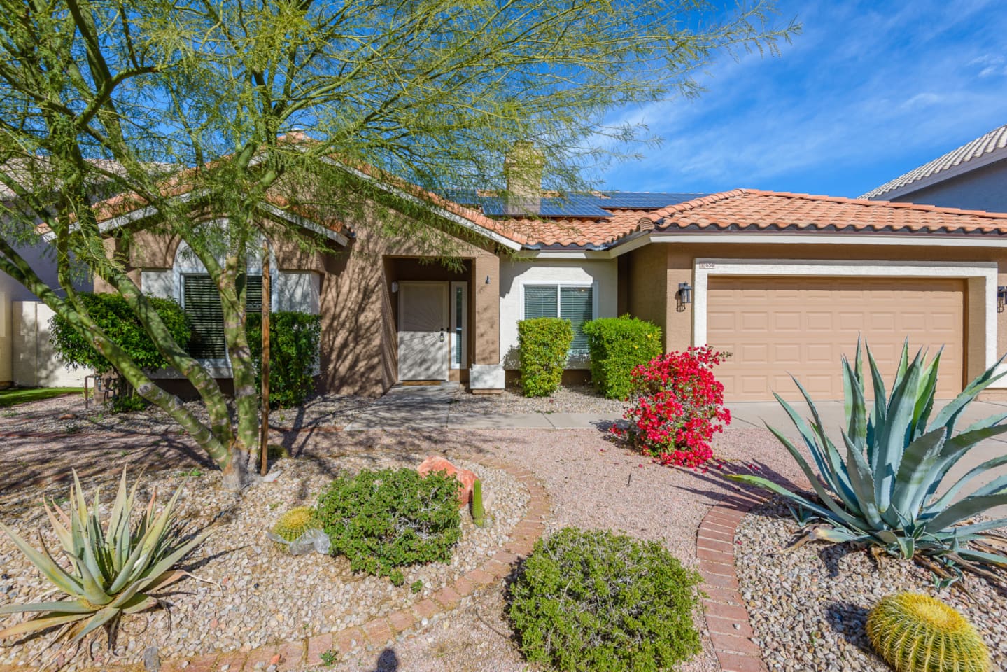 Front entry view with mature desert landscaping, paved walkway, and easy garage access.