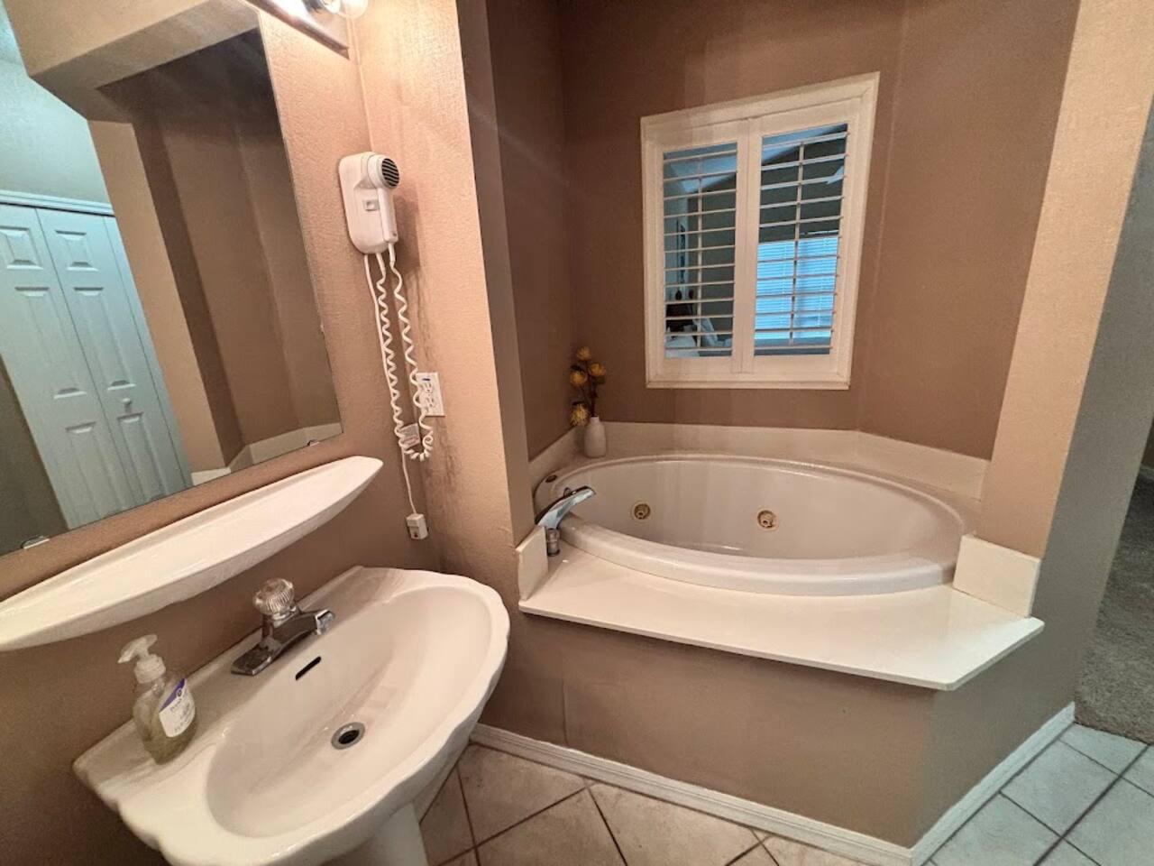 Bathroom with a soaking tub, pedestal sink, and bright natural light from the window.