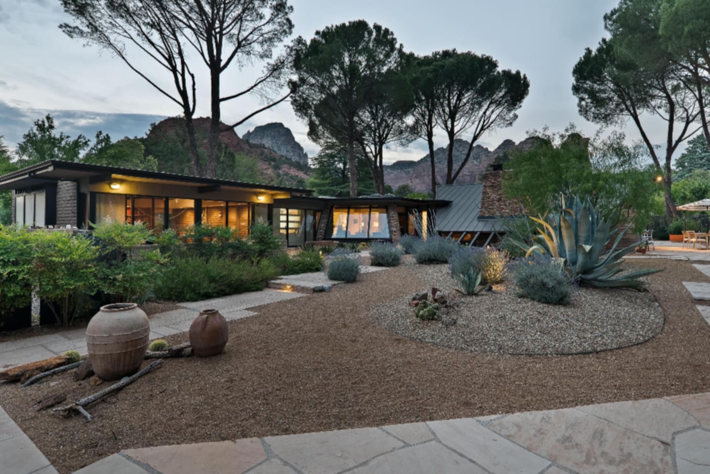 Spectacular dusk view of this mid-century sanctuary, nestled among mature pines and framed by Sedona’s iconic red rock formations — where serene desert landscaping meets timeless architectural design.
