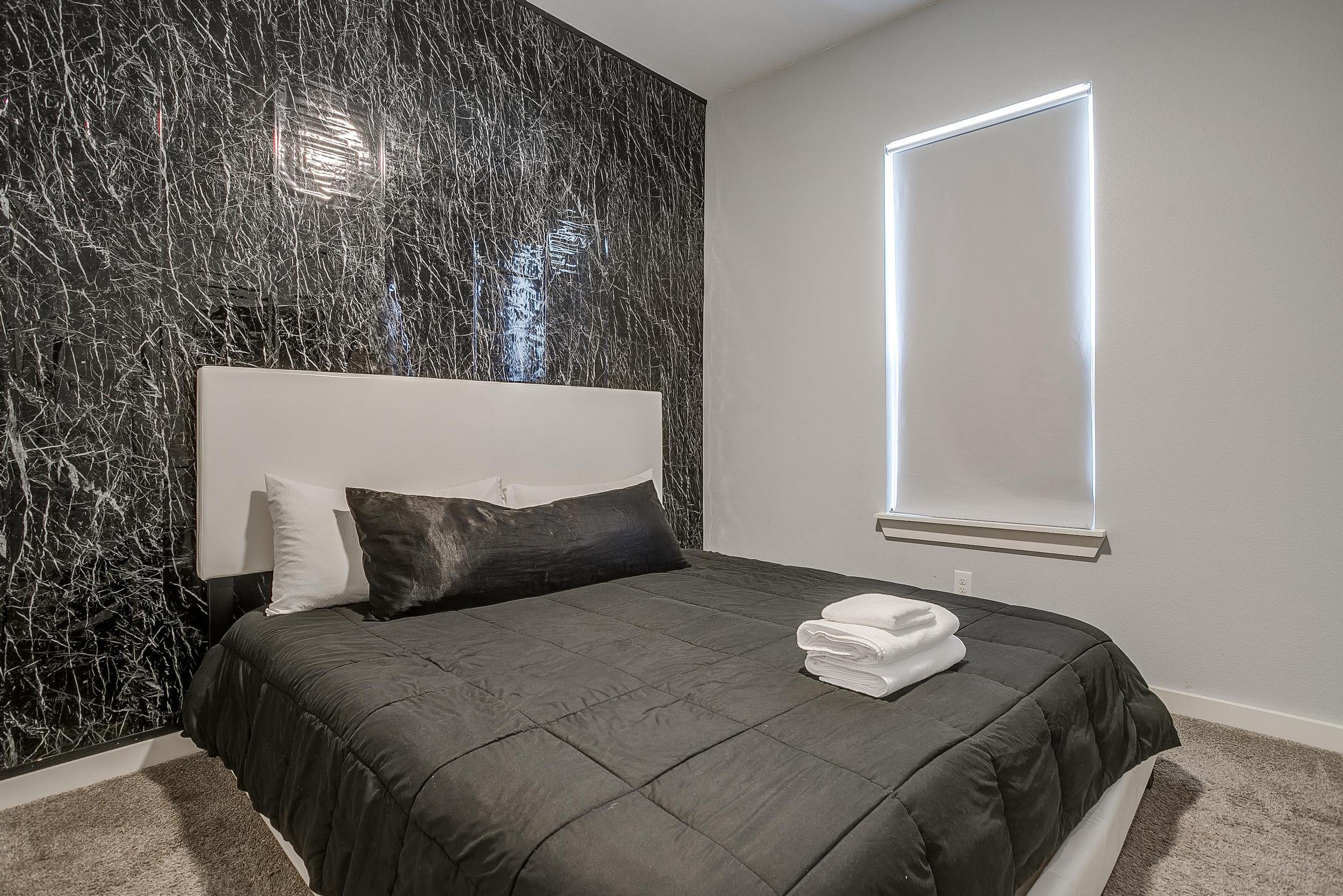 Sleek king bedroom with textured accent wall and blackout curtains. (Bedroom 2 or 3)
