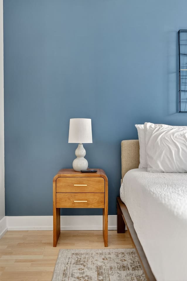 Thoughtful touches add warmth to your stay—soft lighting, modern wood accents, and calming blue walls create a serene bedroom retreat, perfect for winding down after a day in downtown Des Moines.