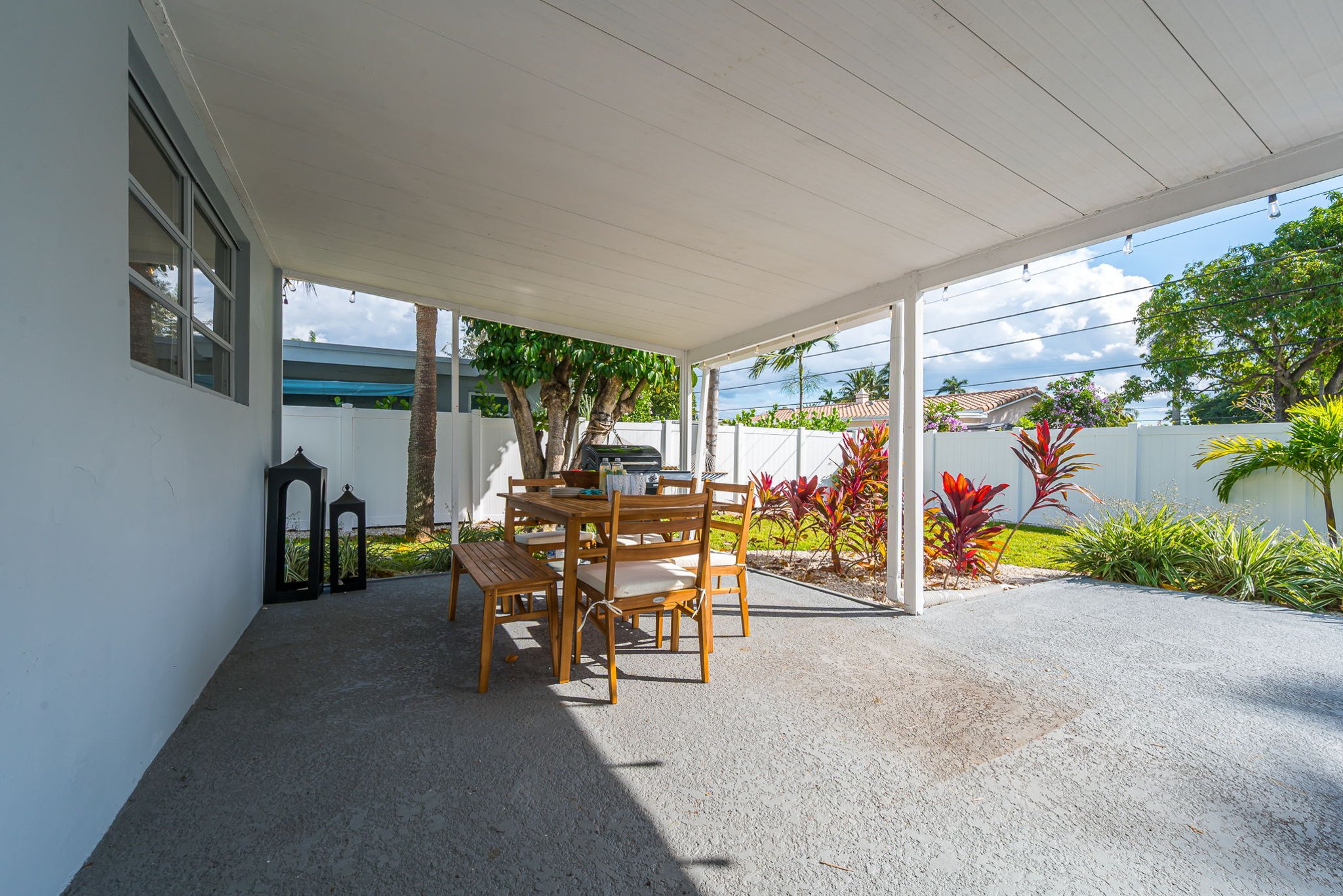 A serene covered patio with chic seating, alfresco dining, a gas grill, and a two-person hammock, all framed by a mix of manicured turf and lush lawn—your private outdoor retreat.