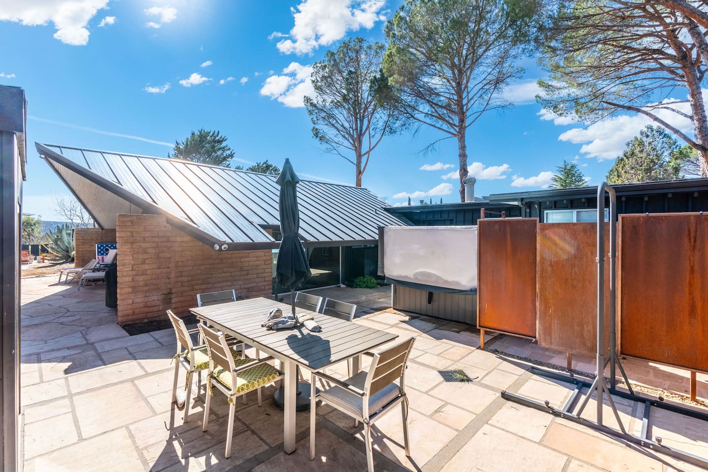Private outdoor dining patio with modern privacy panels, hot tub, and sleek mid-century architecture.