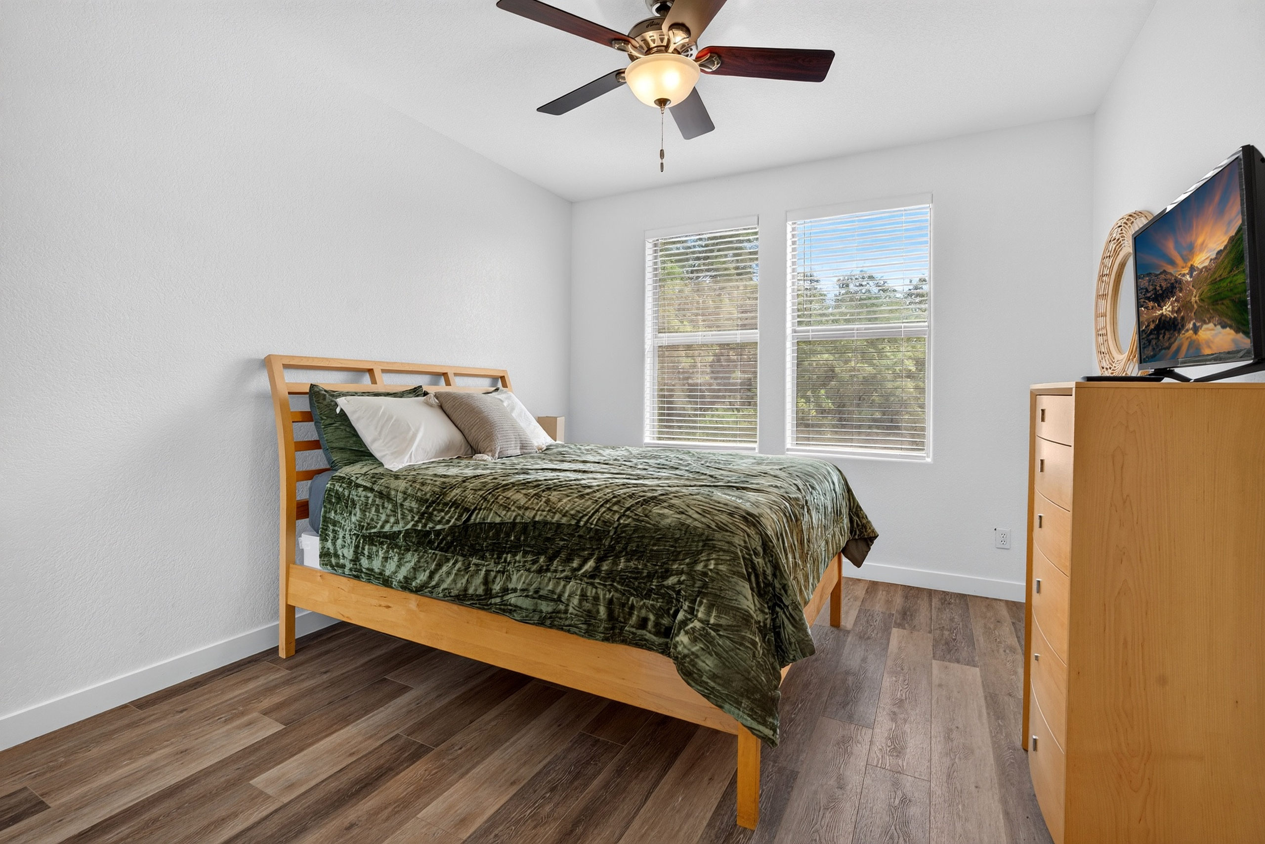 Queen bedroom with dresser storage, TV, ceiling fan, and natural light for a comfortable stay.