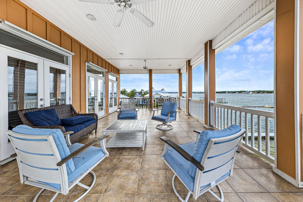 Covered porch with plush loveseat and chairs framing open Little Lagoon water views