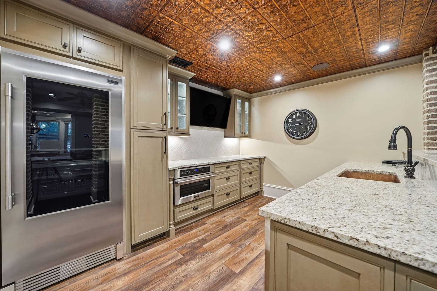 This luxurious kitchenette is designed for easy living, featuring a TV, sink, full fridge, and beverage cooler. Perfect for preparing light meals, grabbing refreshments, or enjoying a cheerful moment located within the game room.