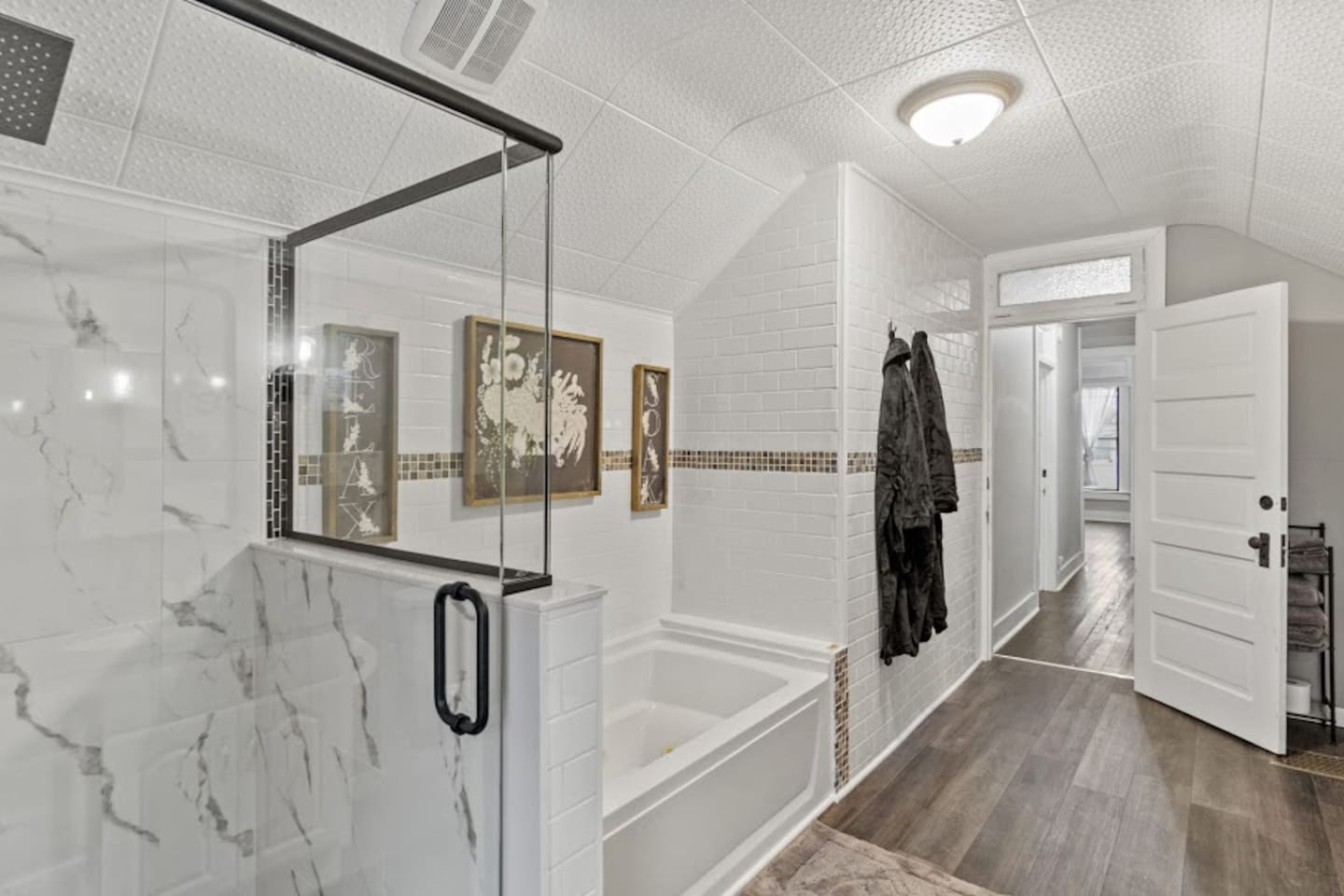 Elegant full bathroom featuring a glass-covered shower, luxurious bathtub, modern lighting, stylish picture frames, and sleek flooring—designed to blend functionality with sophisticated style for a relaxing and inviting space