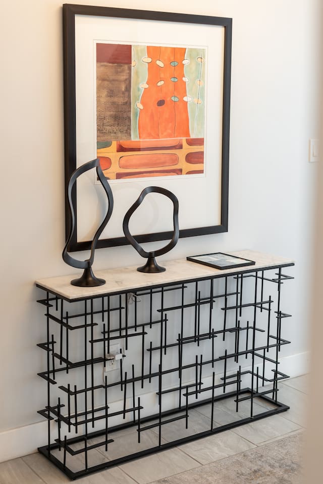 A bold console table with sculptural black decor and vibrant art pieces adds a curated touch to the entry experience.
