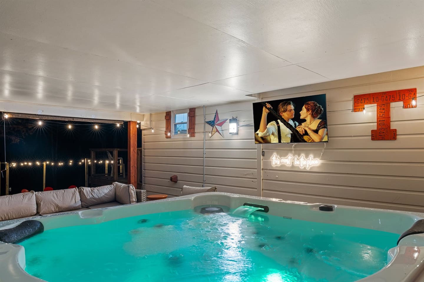 Private covered hot tub with outdoor TV, lounge seating for all, and string lights — the perfect nighttime retreat during your Knoxville stay.