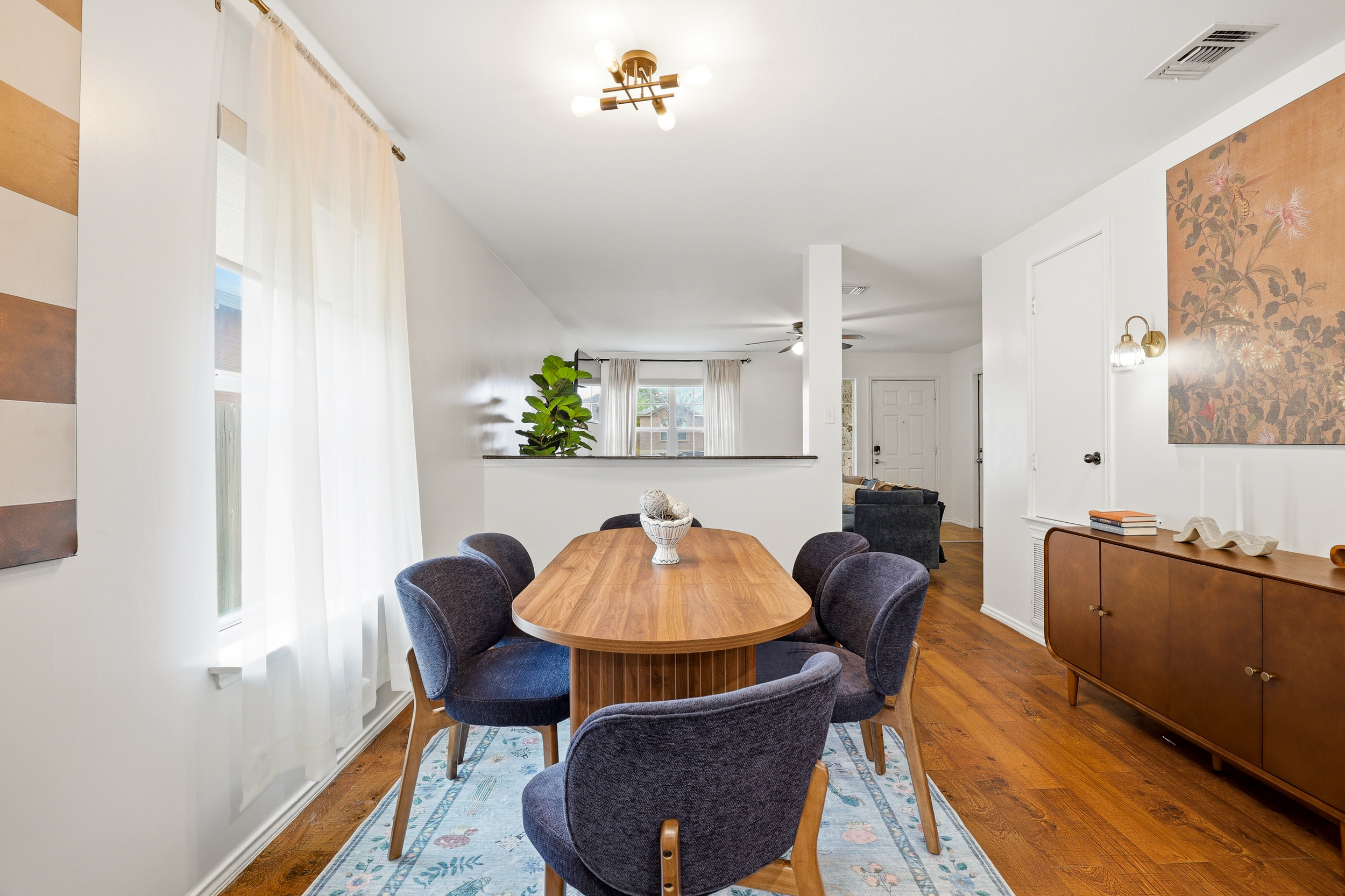 Dining area with seating for 6, mid-century sideboard, large-format botanical art, and warm sconce lighting. Open-plan layout flows directly into the living room for a comfortable, connected group experience.