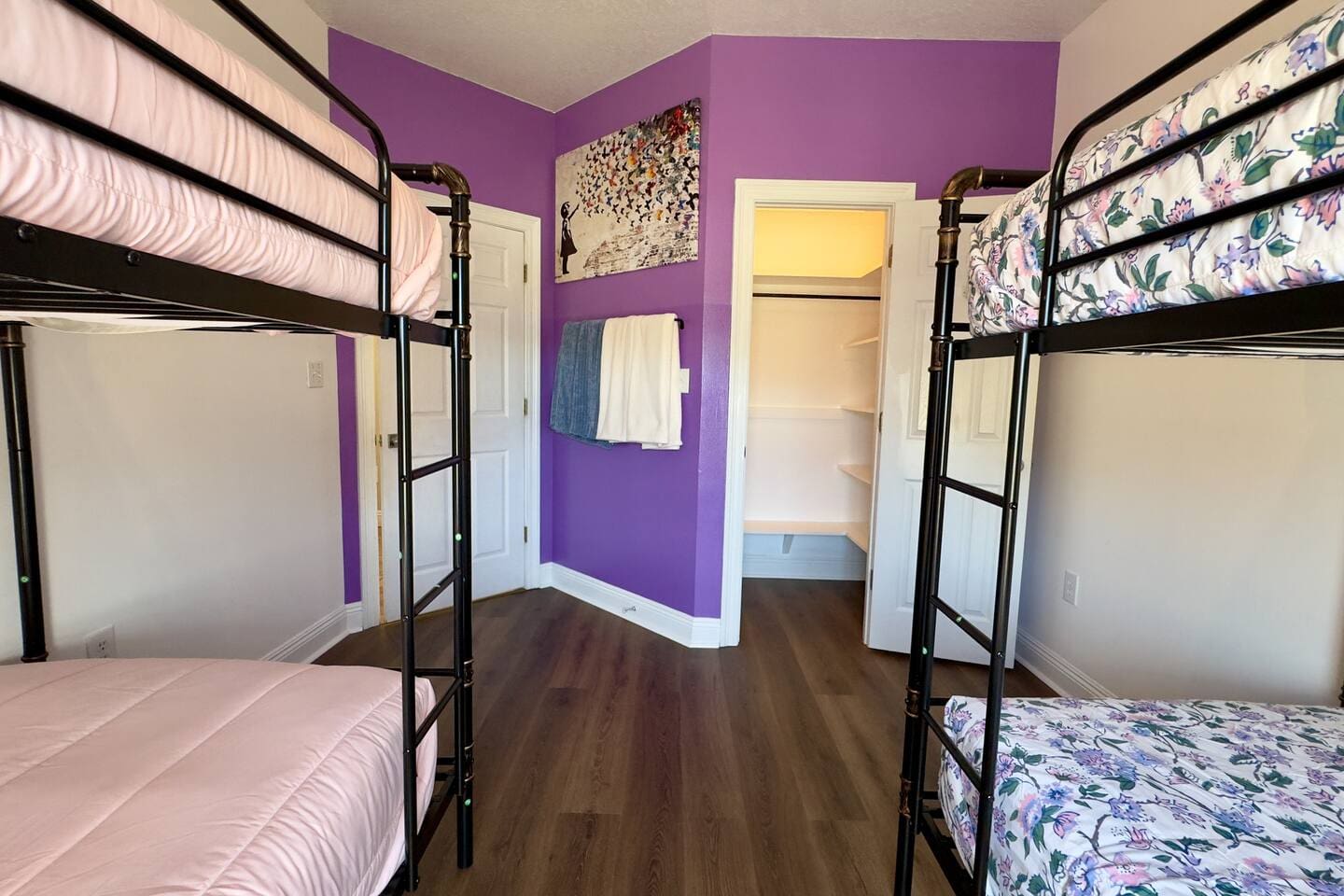 A bold purple wall with abstract artwork and neatly hung towels creates a lively, welcoming vibe.