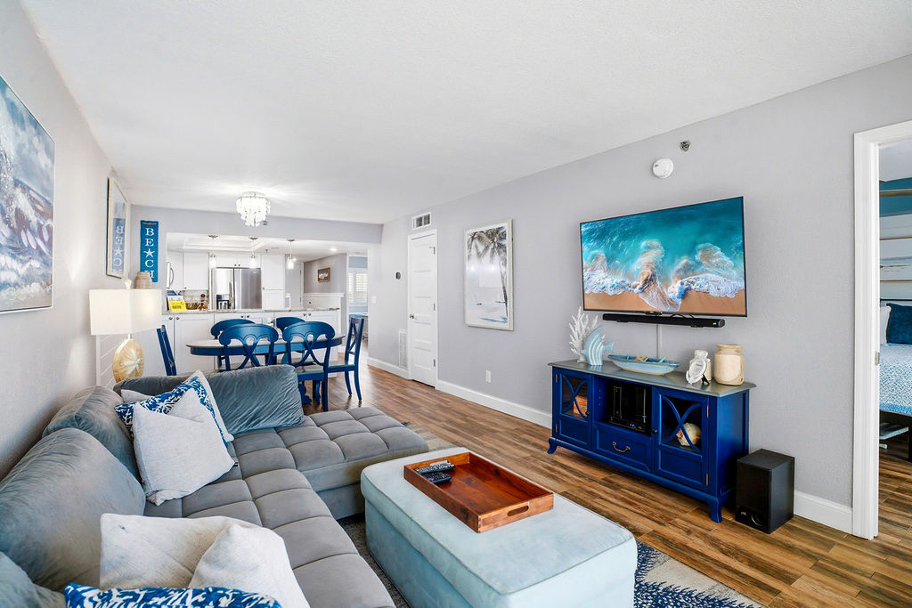 Spacious open-concept living and dining area with comfortable sectional seating, smart TV, and seamless access to the fully equipped kitchen and private bedroom.