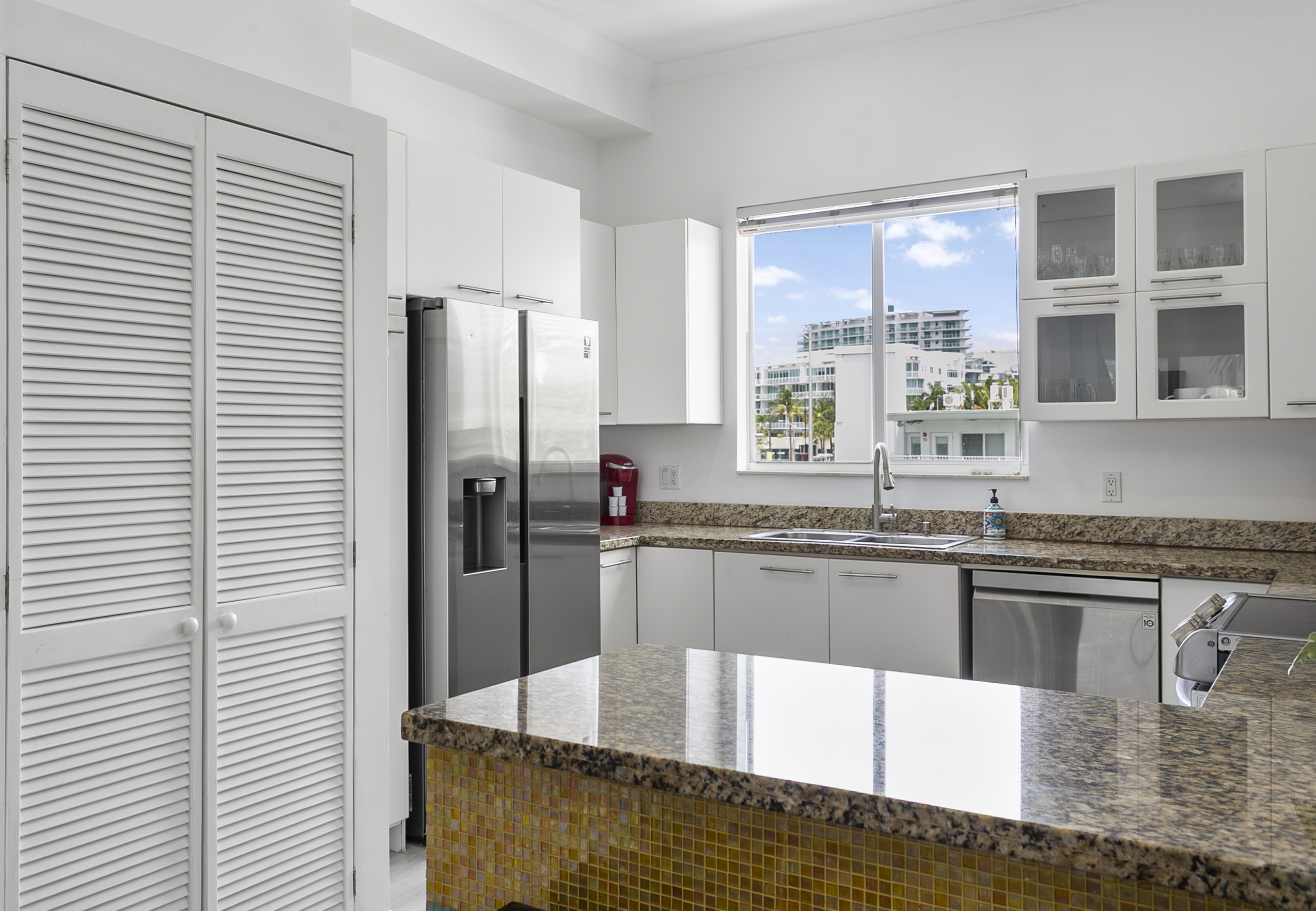 Mosaic tiled kitchen with modern appliances and breakfast counter. LG laundry tower behind closet doors