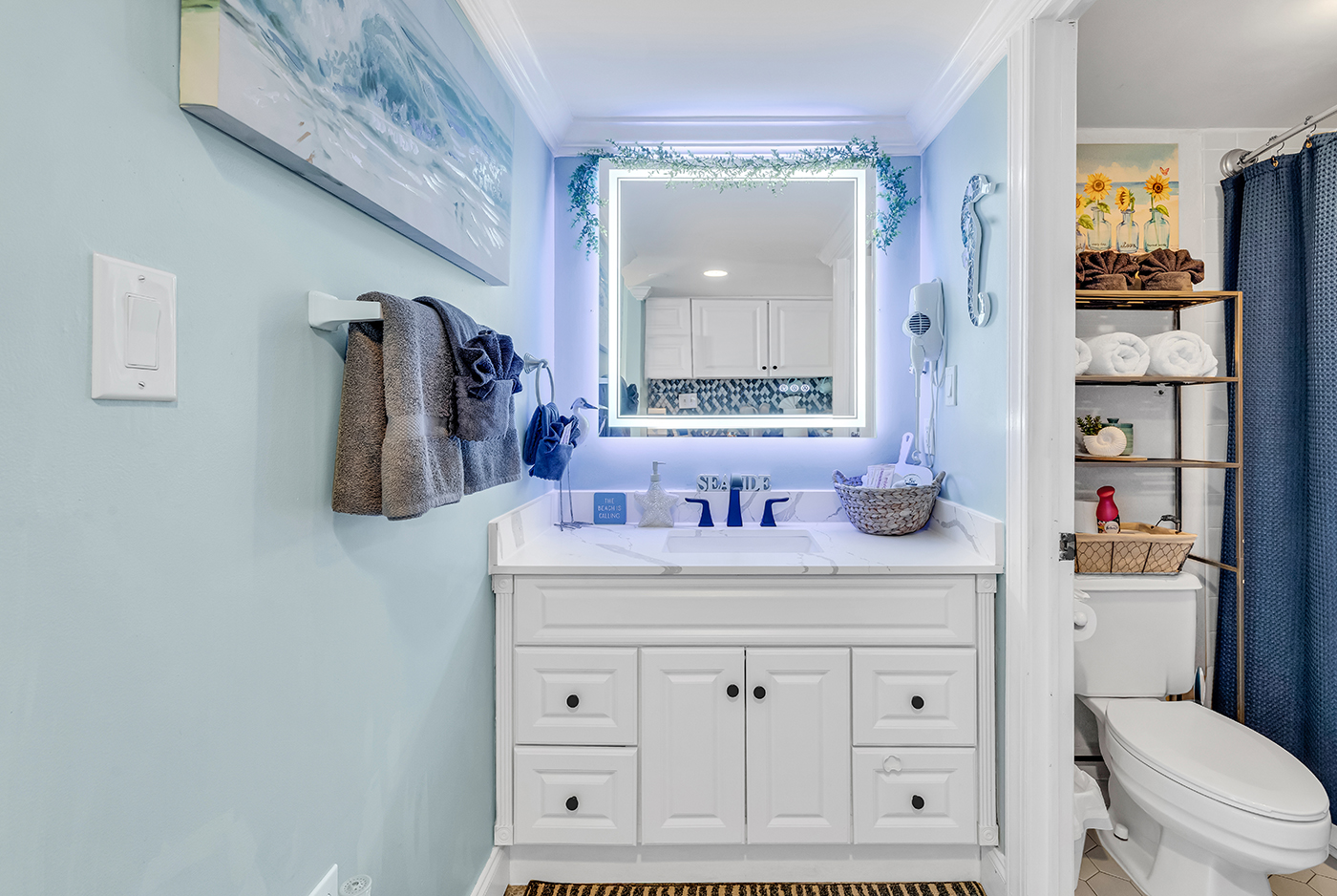 Bathroom featuring glowing LED vanity mirror with storage shelving and fresh towels provided