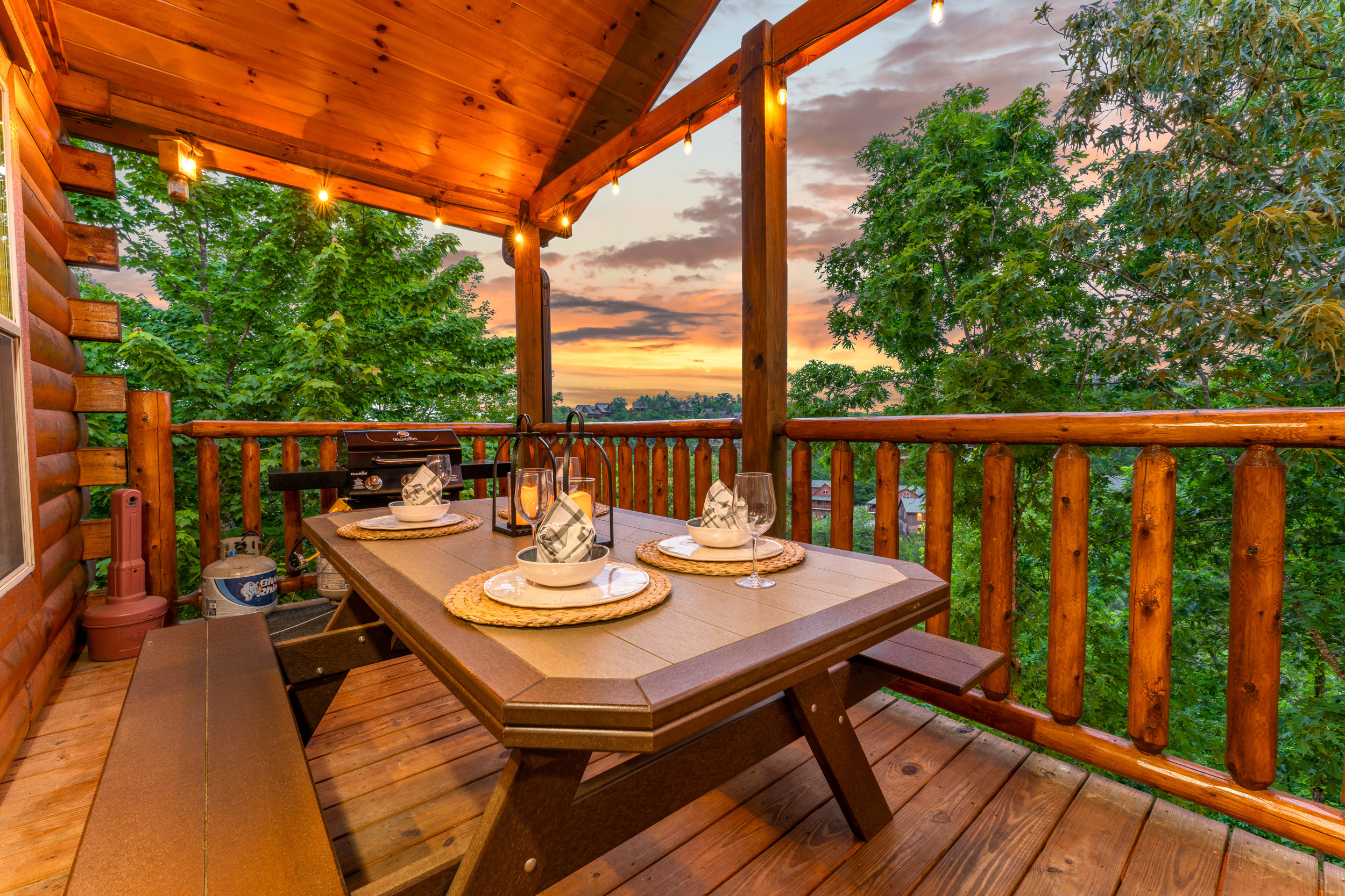 [Balcony, First Floor] Covered deck featuring a gas grill and picnic table with string lights and mountain views of the surrounding resort.