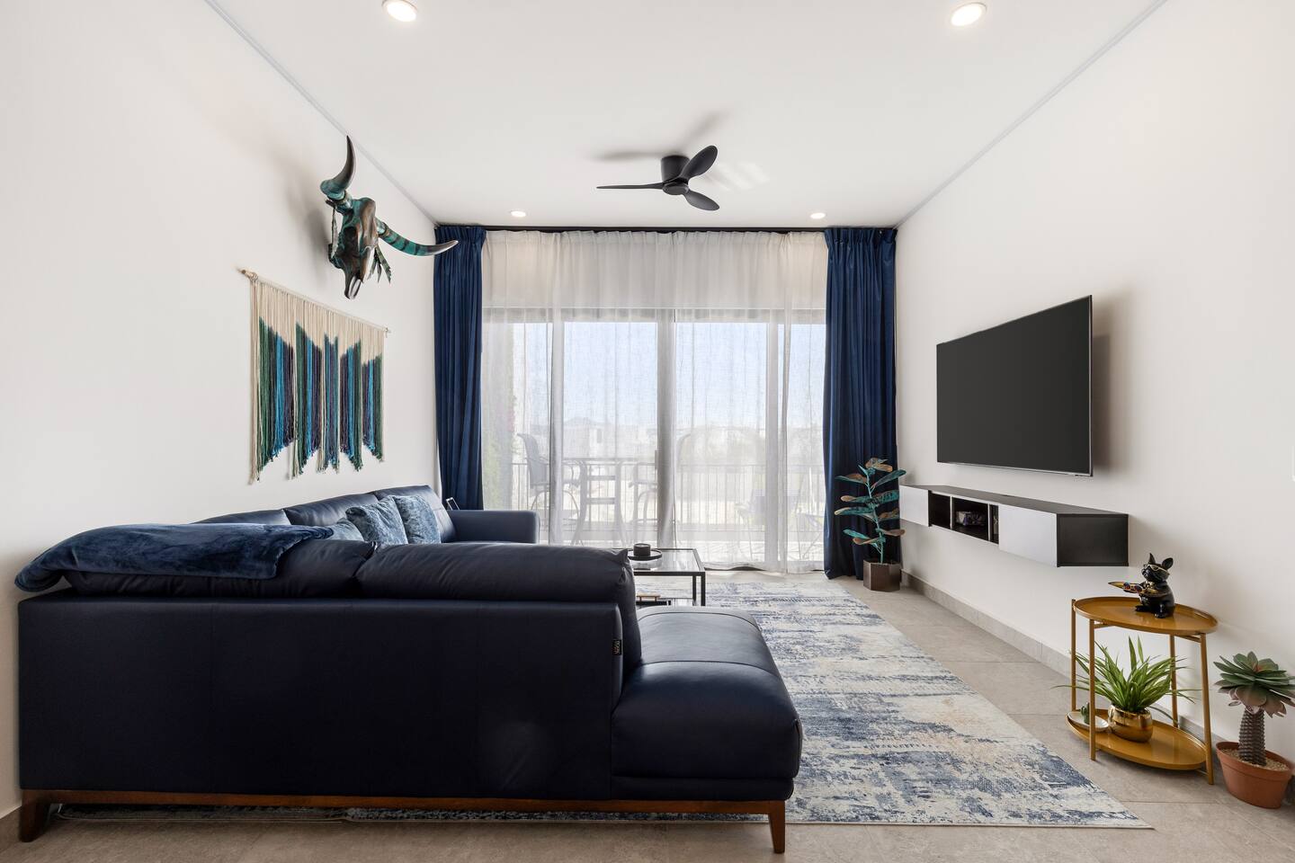 Relax in the living room facing out to the balcony, showcasing stunning local artist wall art and a luxurious left-facing blue BOAL Italian leather sectional.